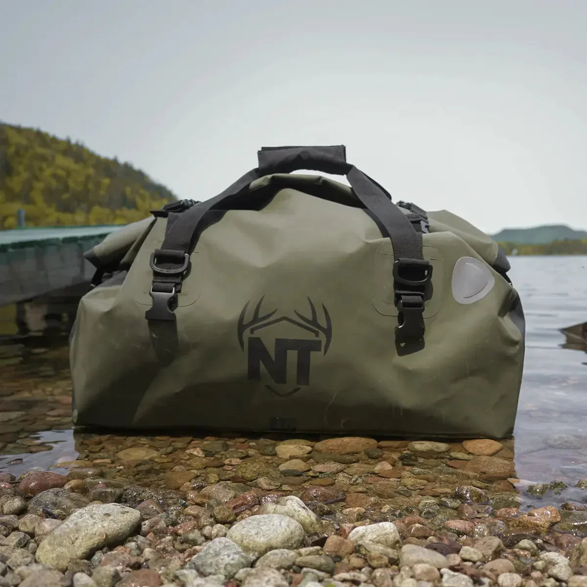 Green waterproof weekender bag with NT antler logo on rocky lakeshore outdoors