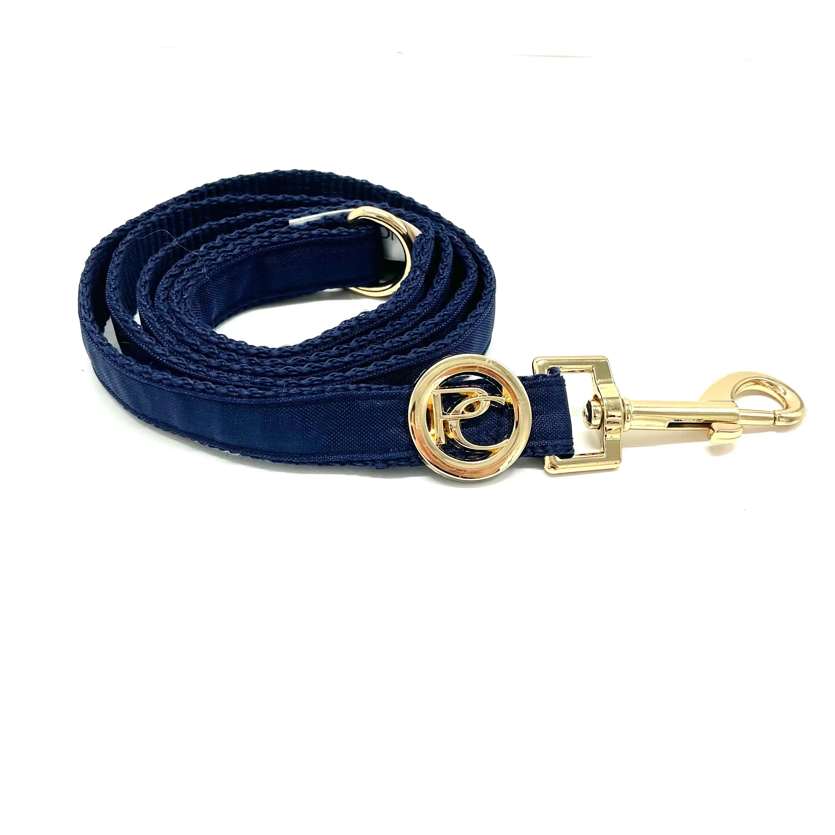 Navy blue dog leash with gold metal clip and decorative gold round logo on white background