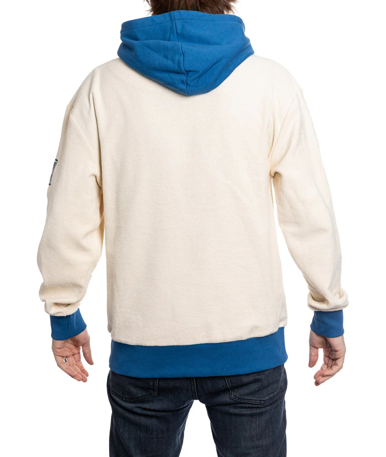 Back view of cream hoodie with blue hood, cuffs, and hem, worn by a person in jeans
