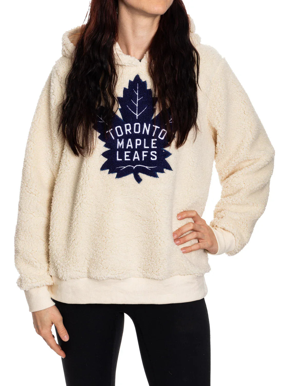 Woman wearing cream Toronto Maple Leafs sherpa hoodie and black leggings on white background