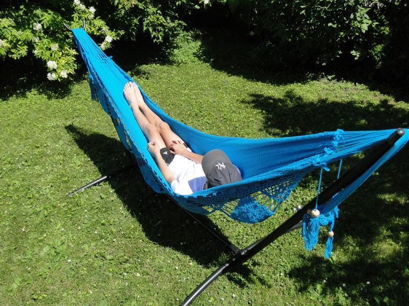 Person relaxing on bright blue hammock with stand in sunny green garden