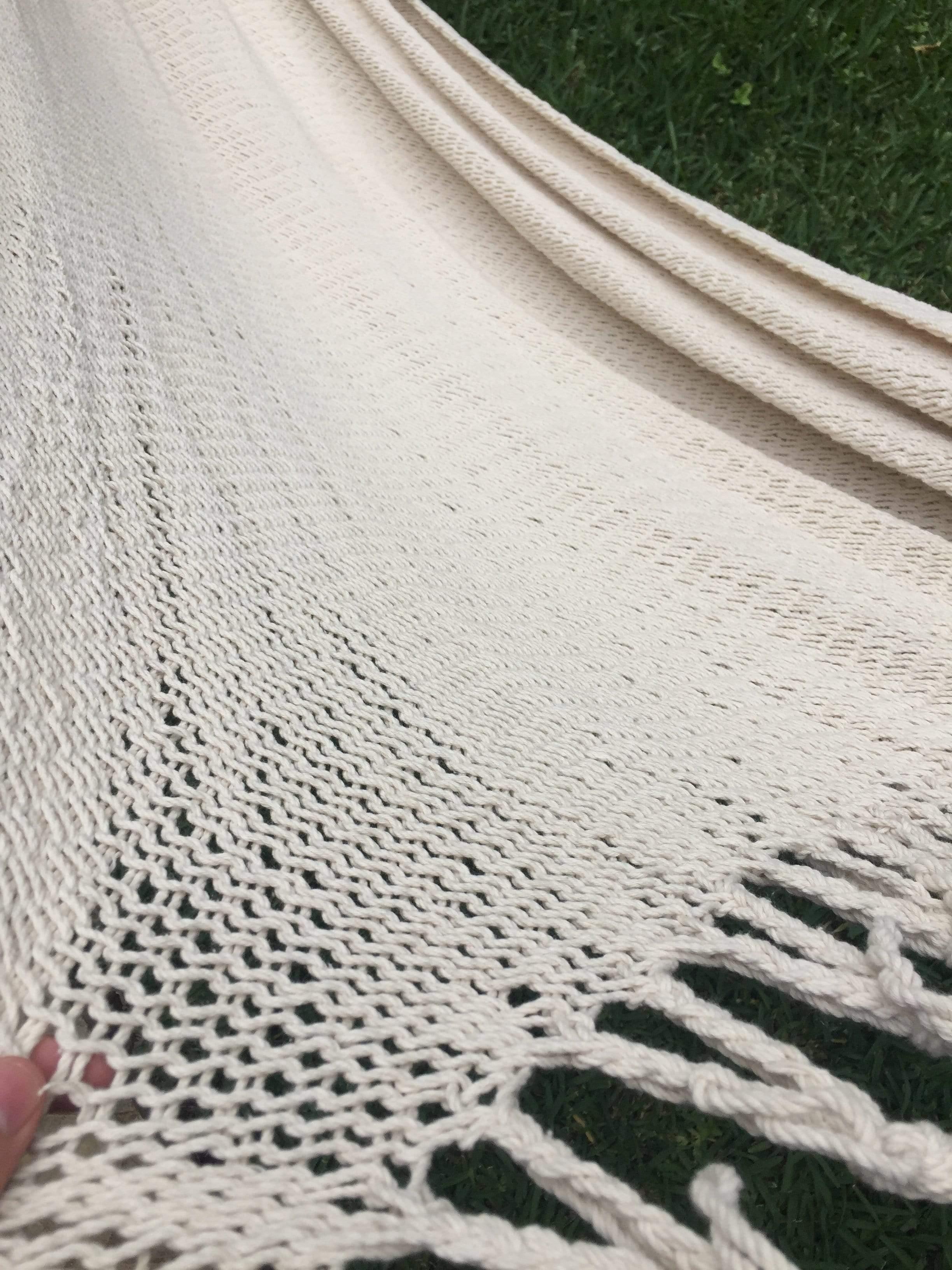 Handwoven cream cotton hammock with fringe detail outdoors on green grass