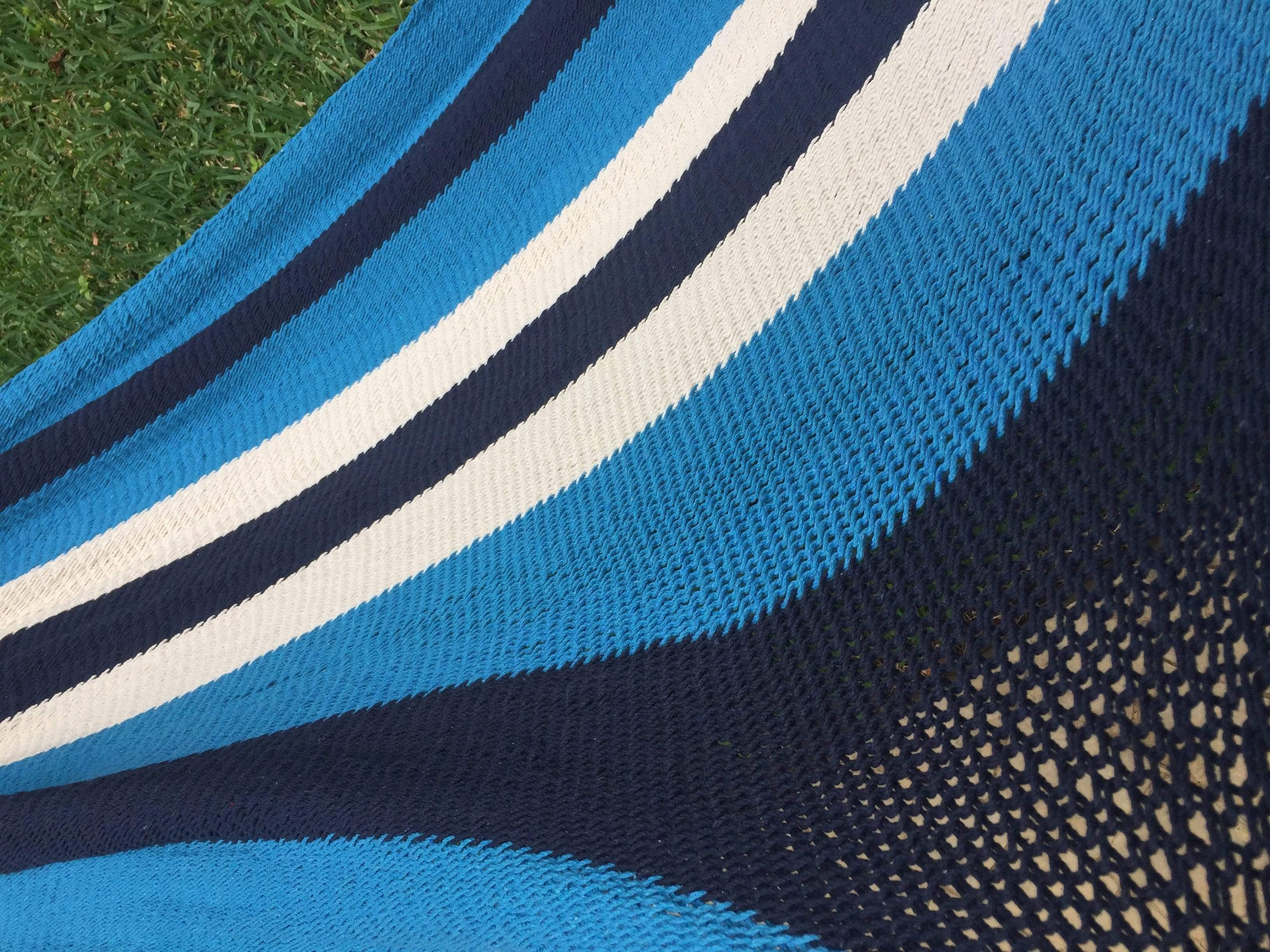 Blue and white striped woven hammock on green grass outdoors