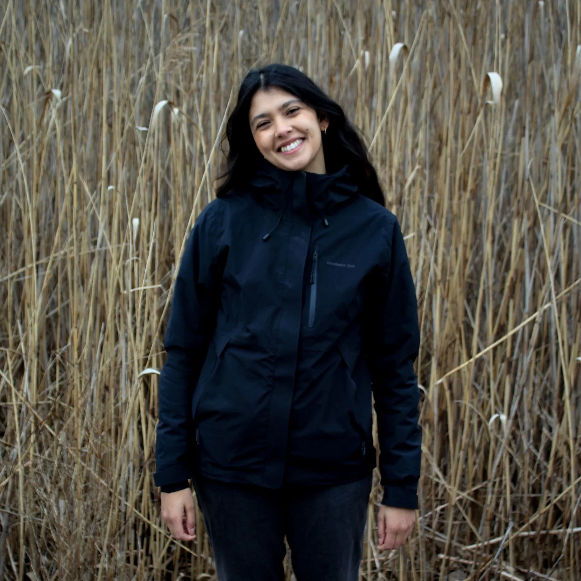 Woman wearing black 3-in-1 fall jacket standing in tall dry grass outdoors
