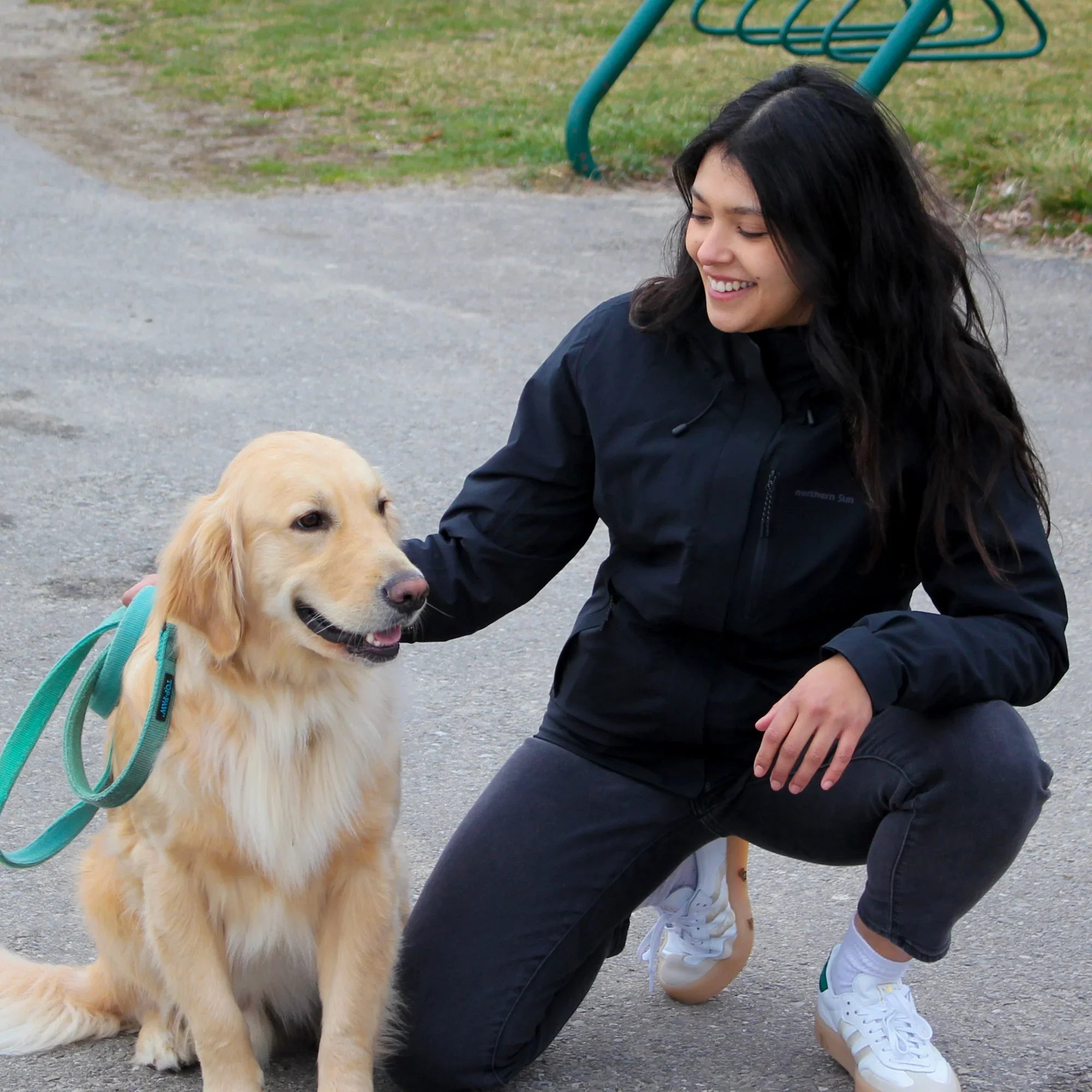 Woman in black 3-in-1 jacket walking golden retriever outdoors on pavement