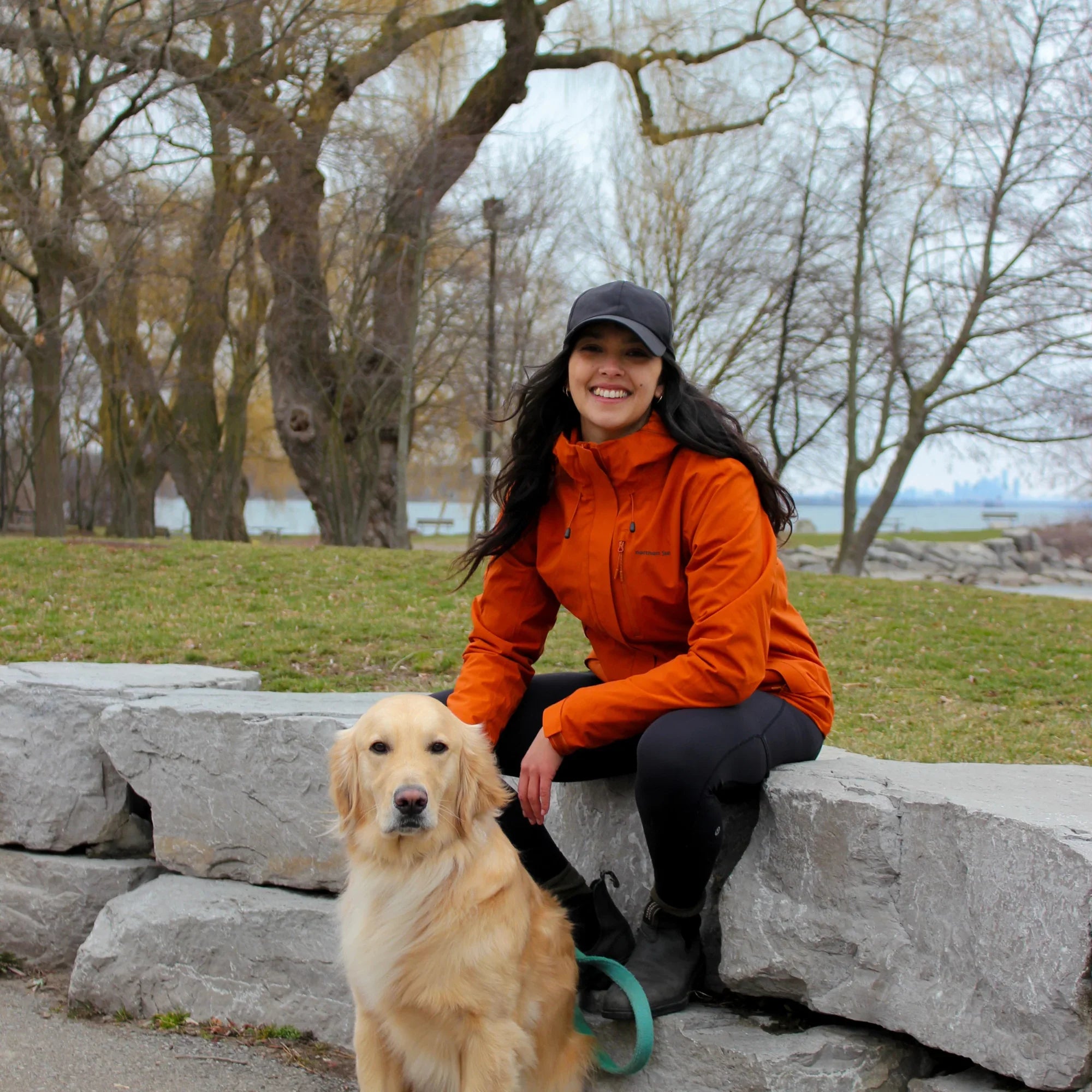 Woman in pumpkin yellow 3-in-1 winter jacket sitting outdoors with golden retriever