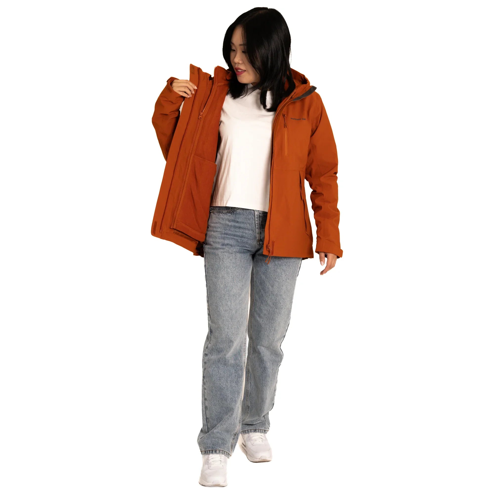 Woman wearing orange waterproof jacket, white shirt, blue jeans, and white sneakers