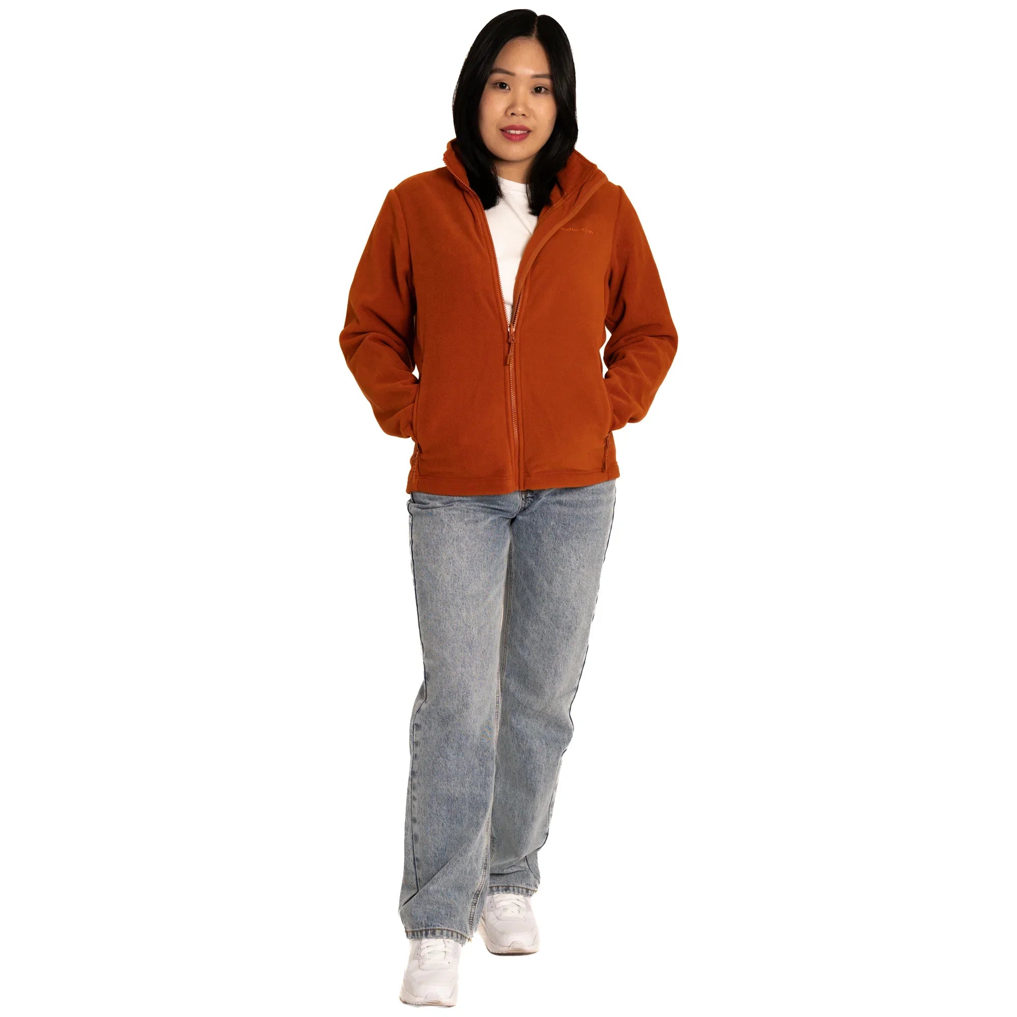 Woman in orange fleece jacket, blue jeans, and white sneakers on white background