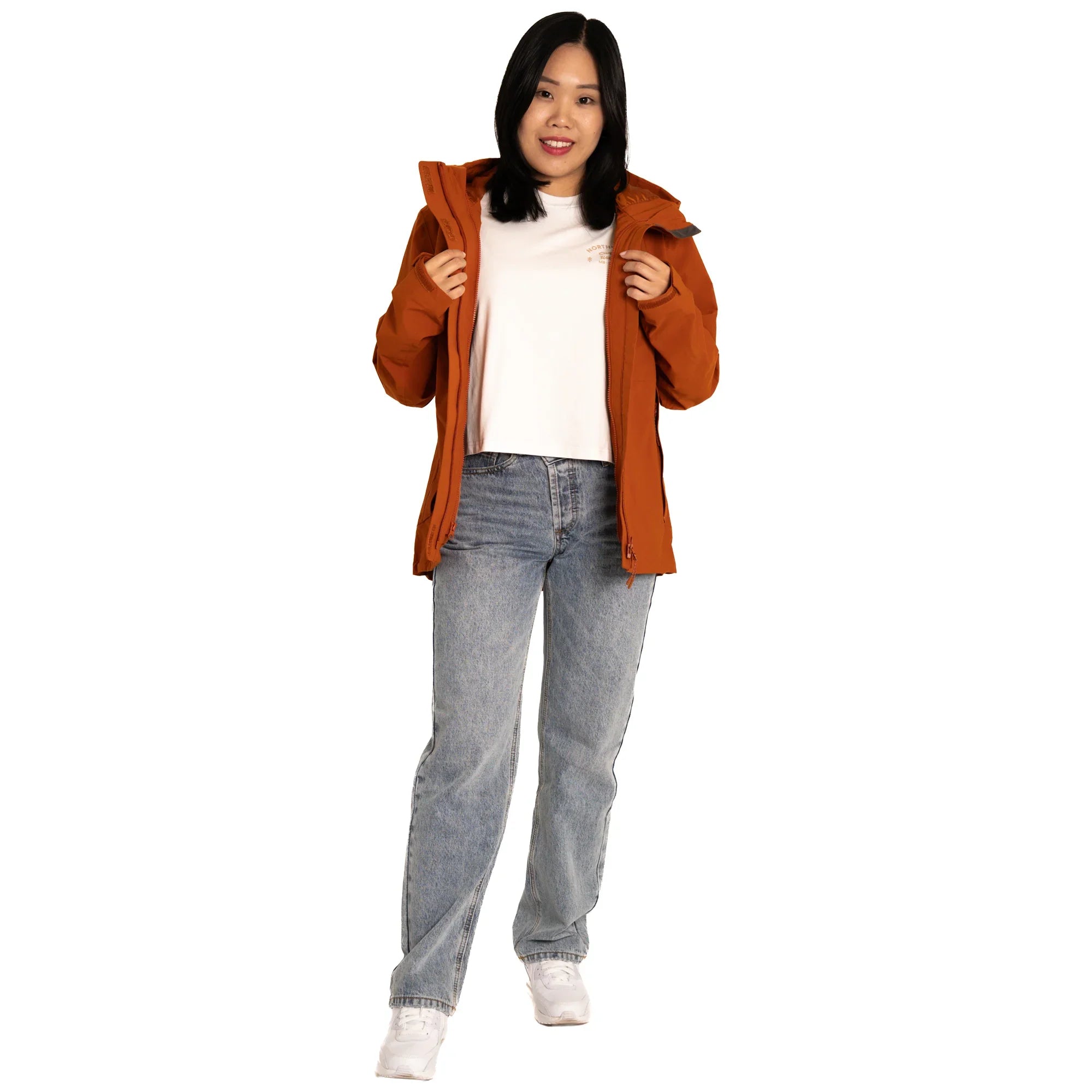 Woman wearing orange jacket, white shirt, jeans, and sneakers on white background