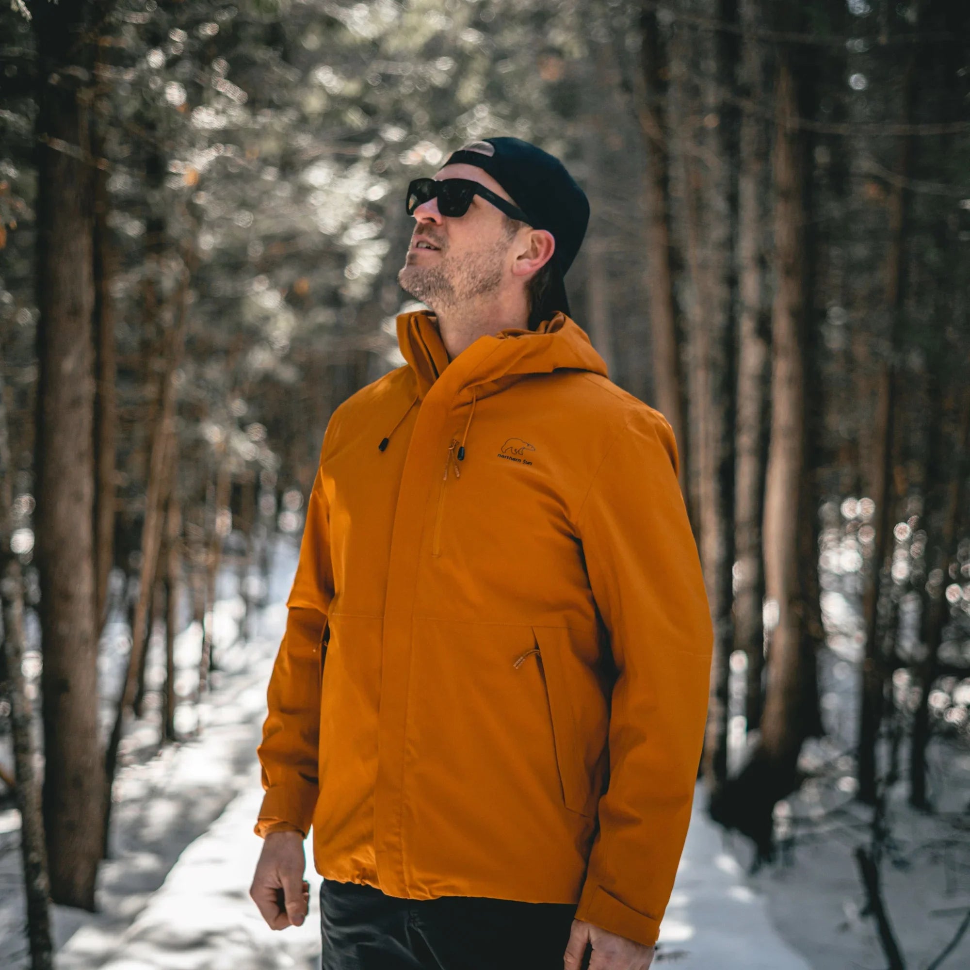 Man wearing orange 3-in-1 winter jacket in snowy forest, outdoor winter clothing