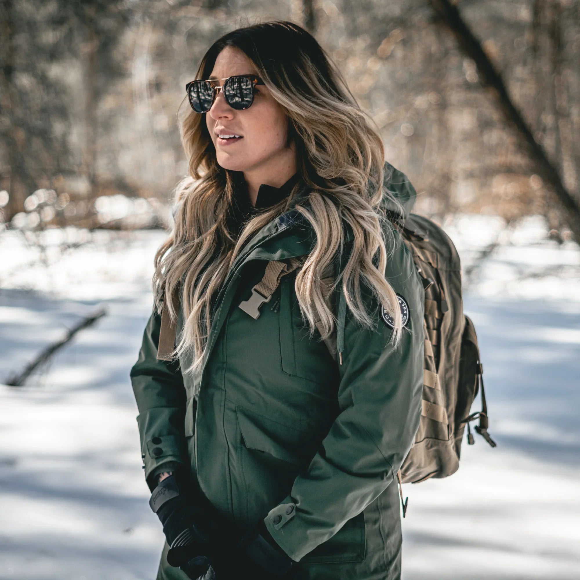 Woman wearing forest green mid-length 3-in-1 winter jacket outdoors in snowy woods