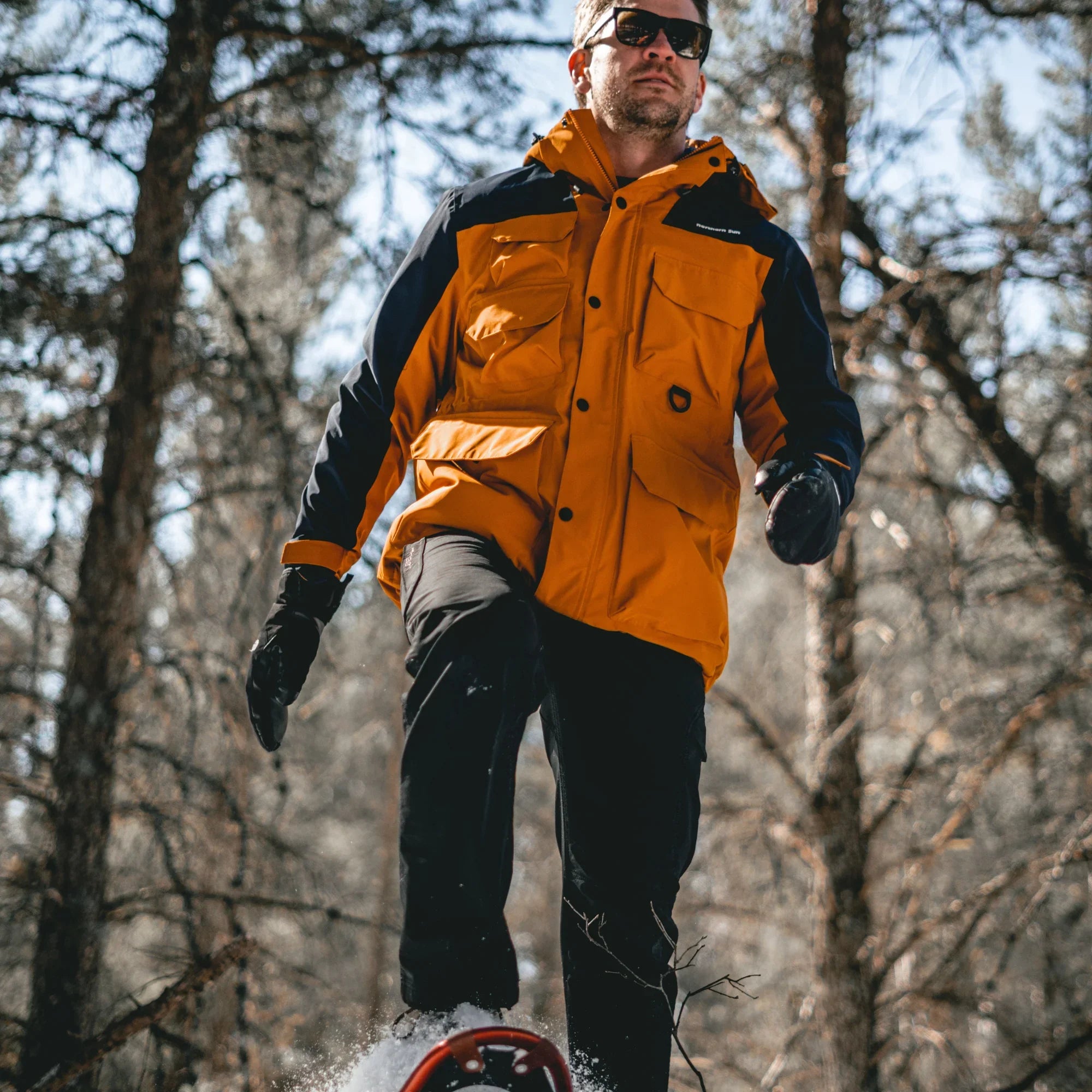 Man wearing orange and blue waterproof 3-in-1 parka hiking in snowy winter forest