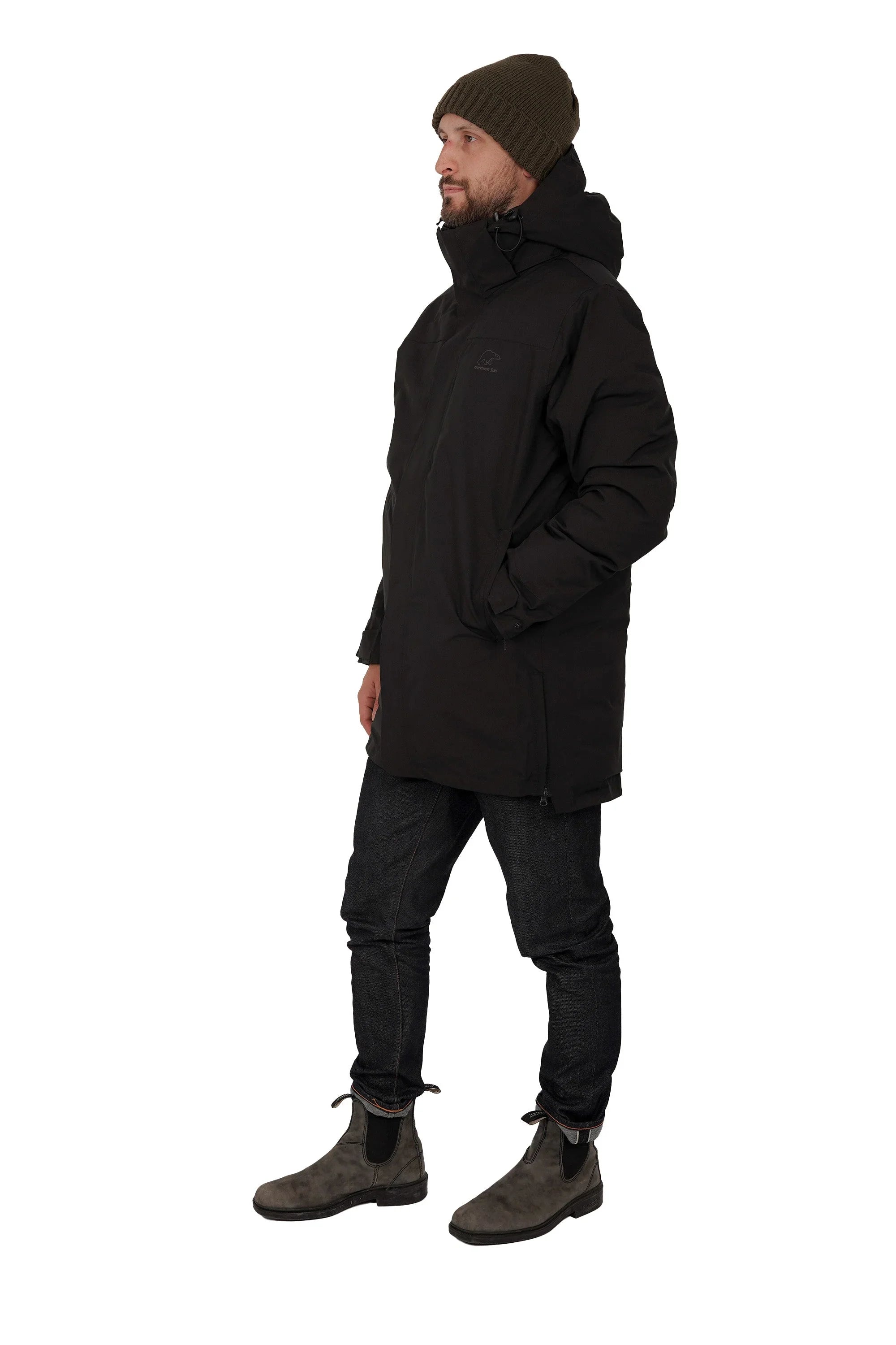 Man in black winter parka, olive knit beanie, jeans, and brown boots on white background