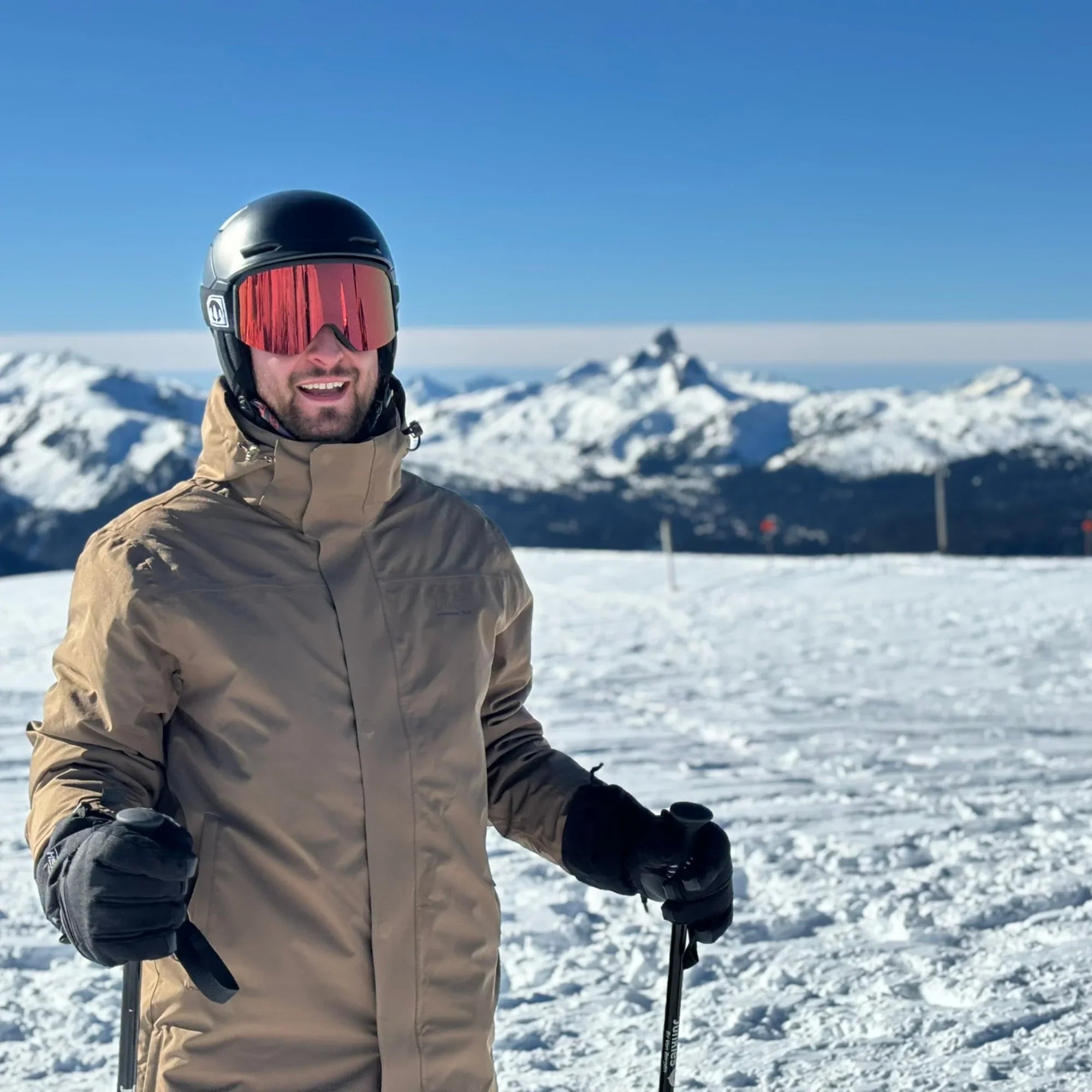Skier in tan jacket and black helmet on snowy mountain with clear blue sky