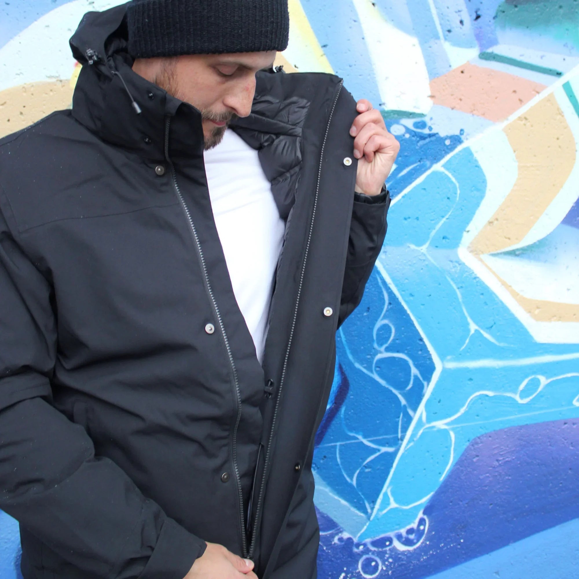 Man in black winter jacket and beanie by colorful graffiti wall