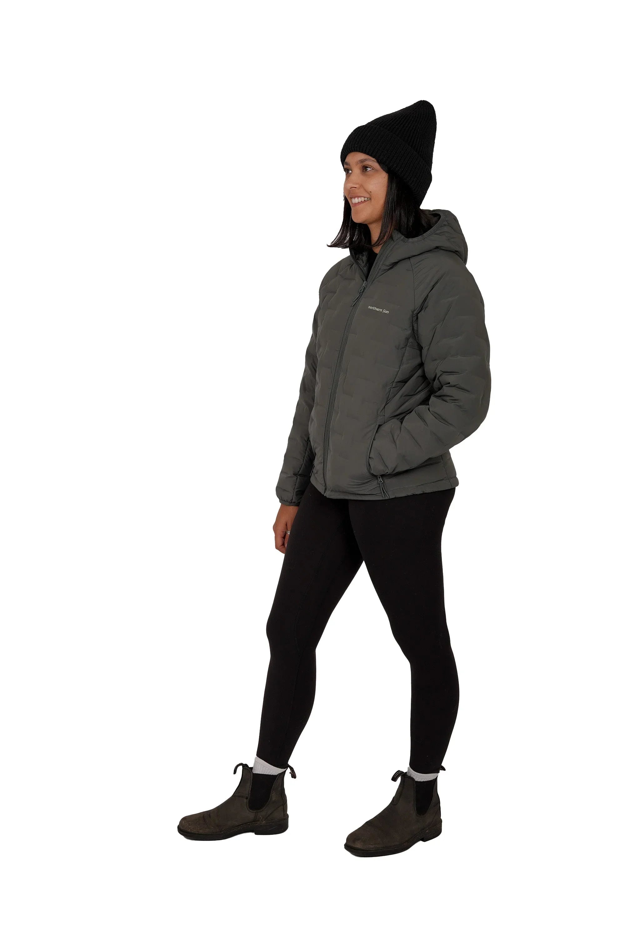 Woman in gray hooded lightweight down jacket, black beanie, leggings, and boots side view