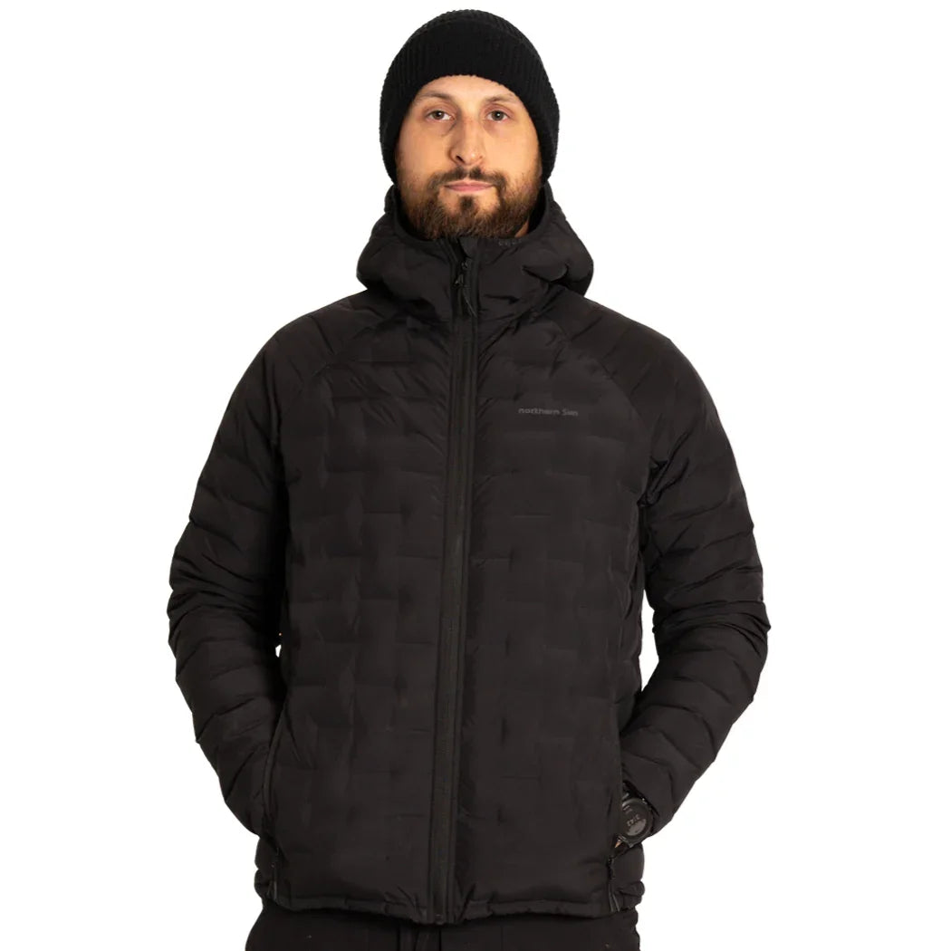 Man wearing black puffer jacket and black beanie, hands in pockets, white background
