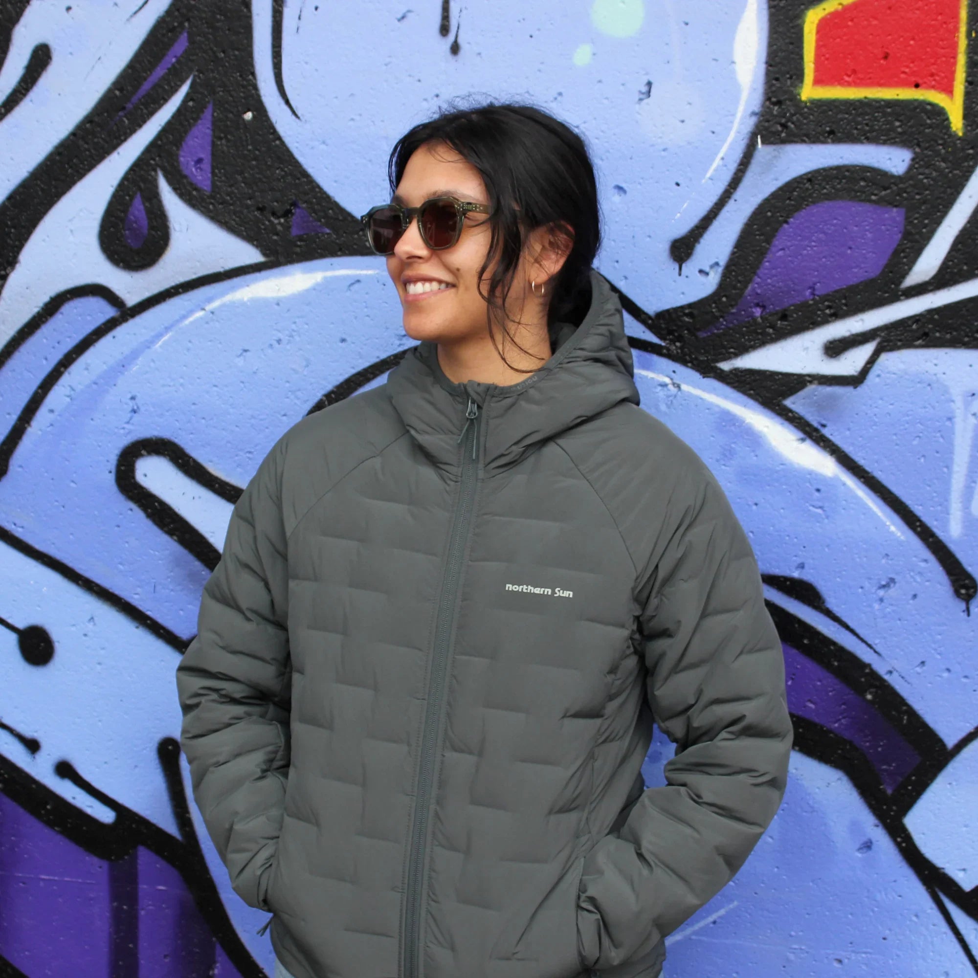 Woman in Northern Sun Dawson lightweight down jacket by graffiti wall, city outdoor fashion