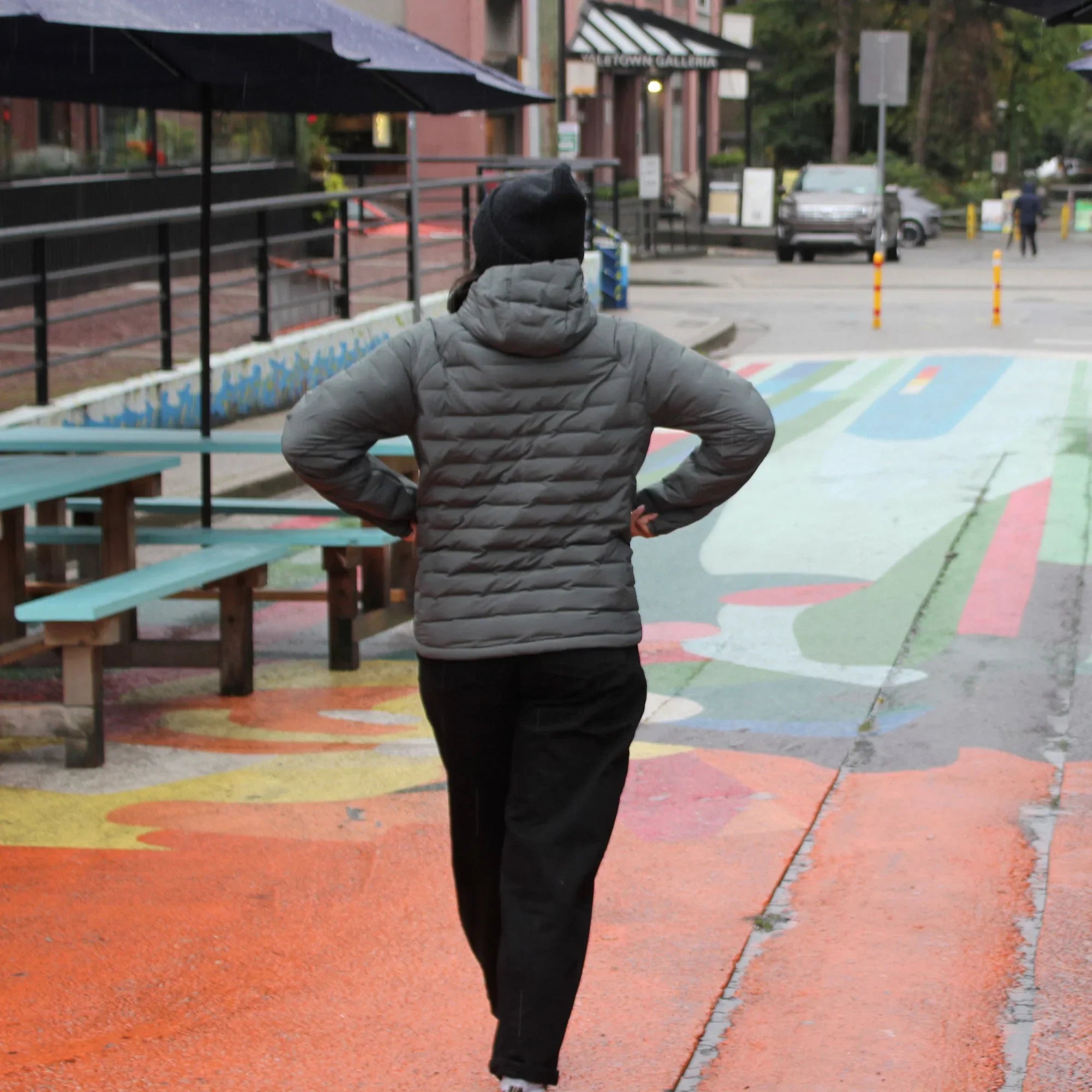 Woman in grey lightweight down jacket walking on colorful urban street with benches