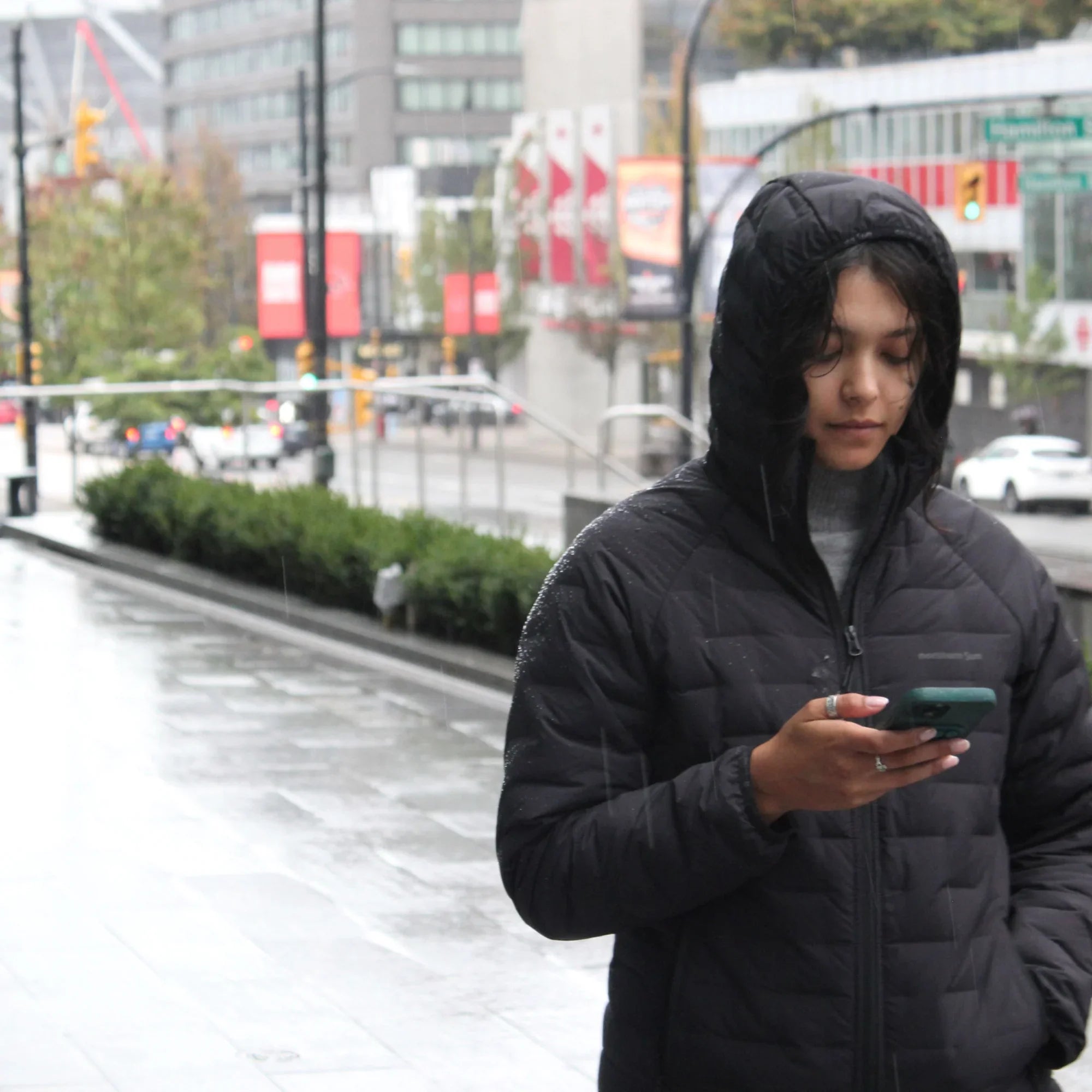 Woman in black waterproof puffer jacket walking in rainy Vancouver city street