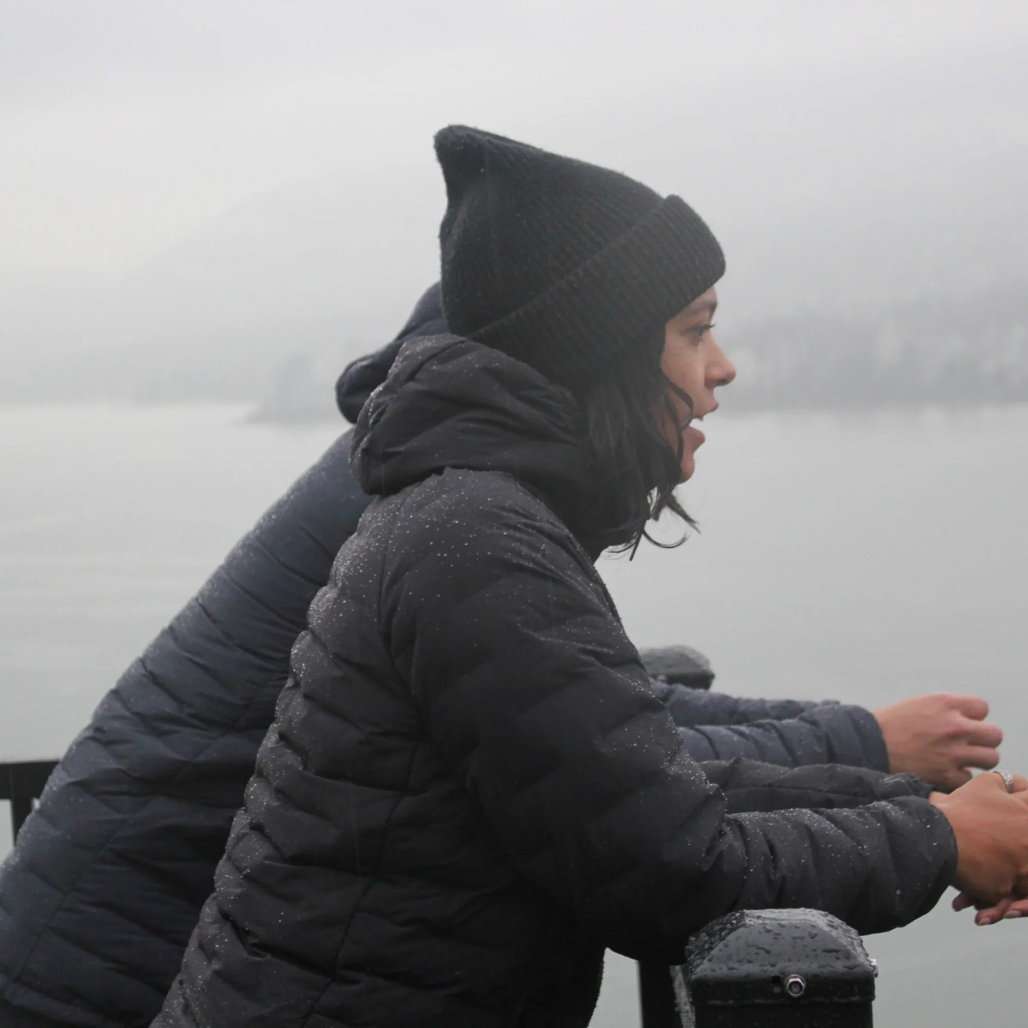 Women wearing water-resistant down puffer jackets and beanie by a misty lake in winter