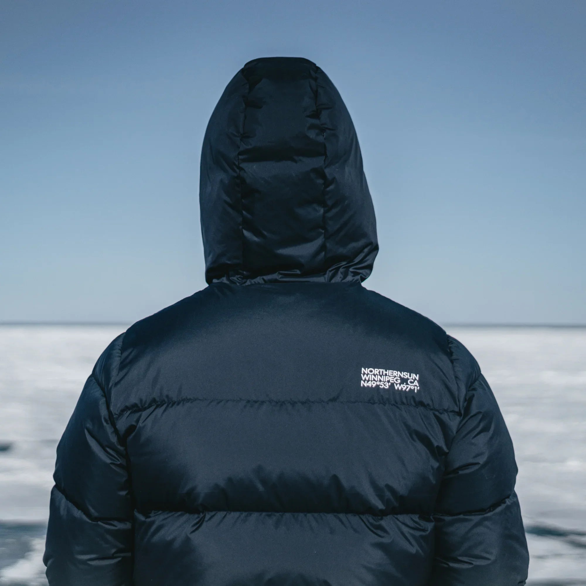 Man wearing black Northern Sun men's winter down parka with hood outdoors on icy landscape