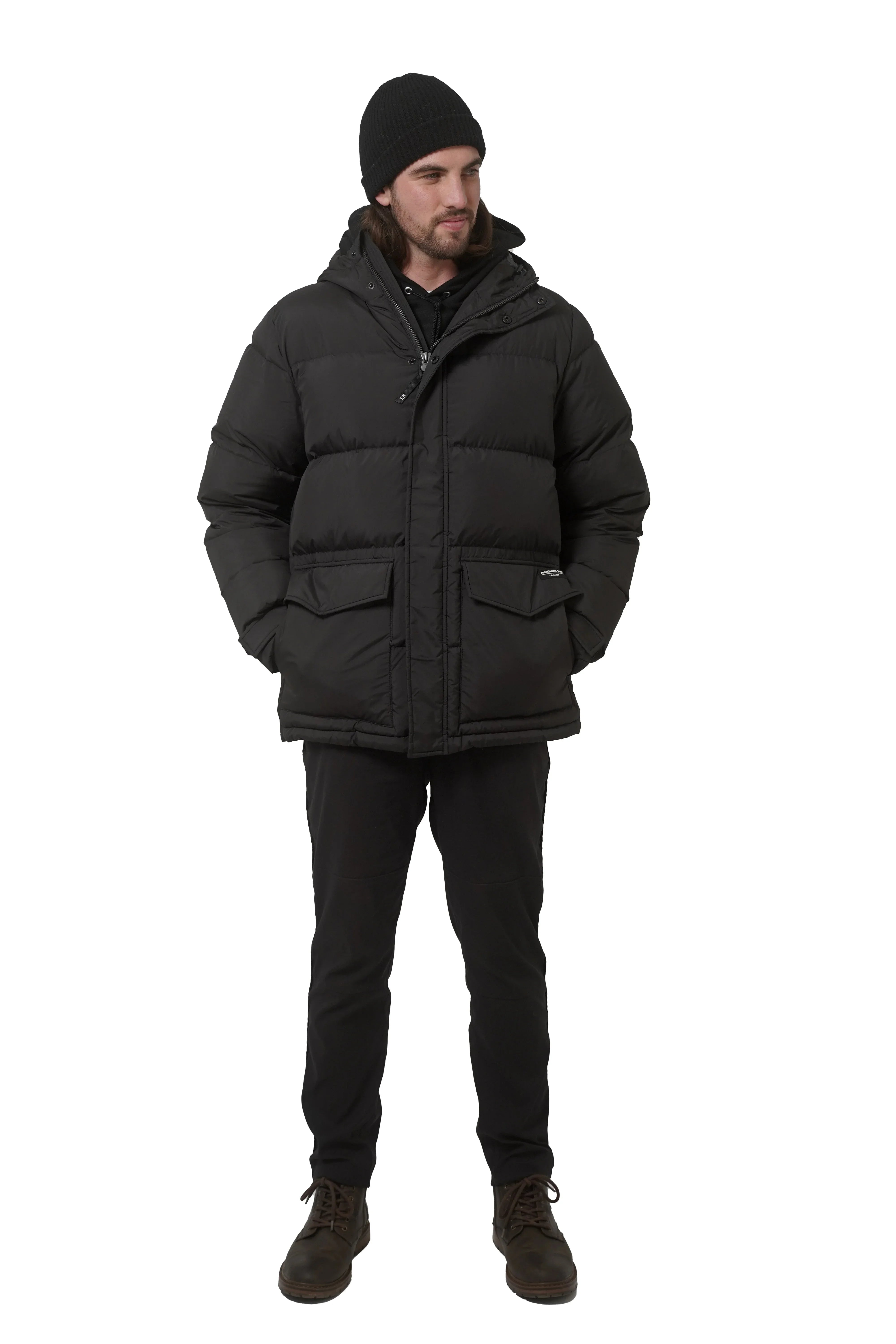 Man modeling black winter down parka, black pants, boots, and knit beanie on white background