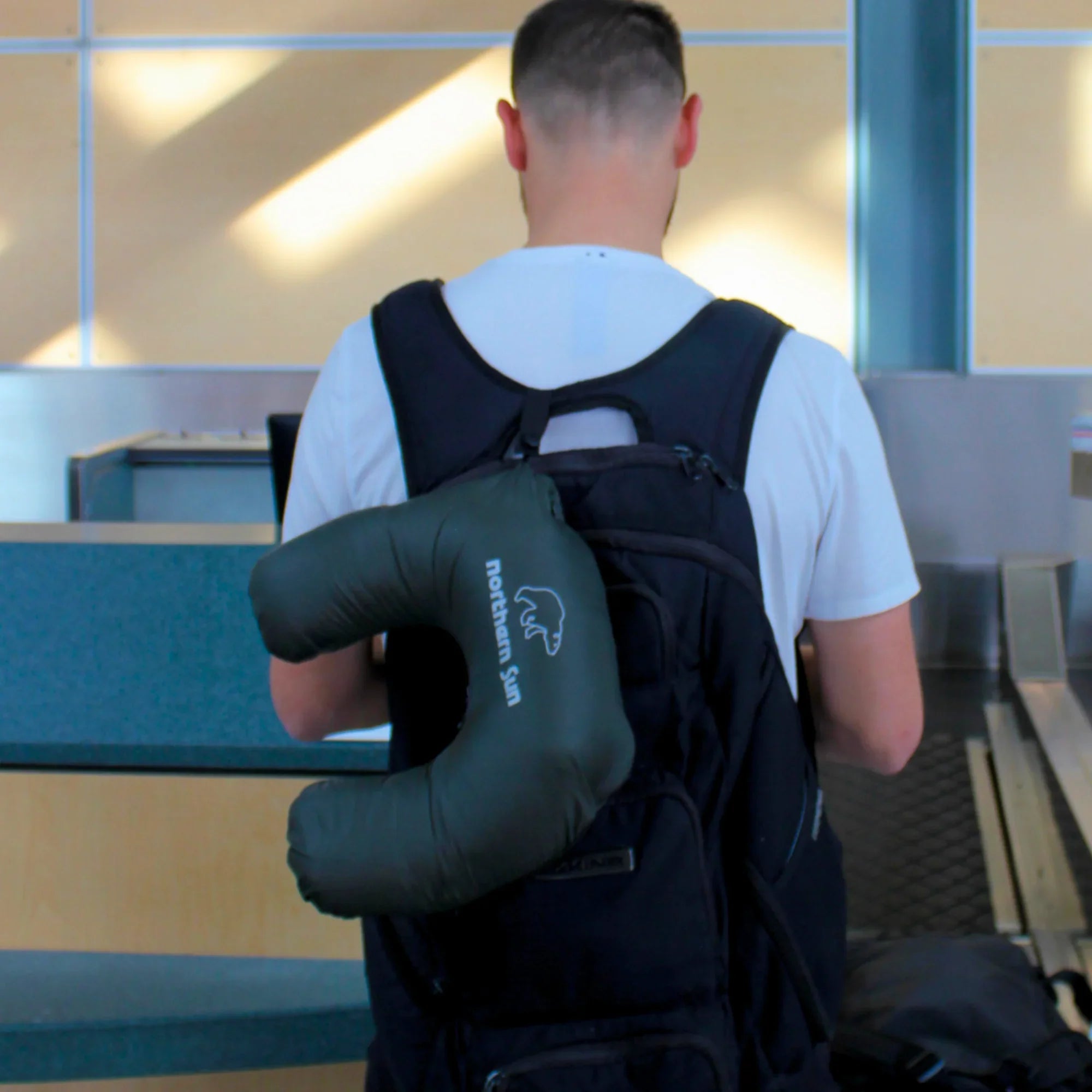 Man at airport with Northern Sun lightweight packable down jacket travel pillow on backpack