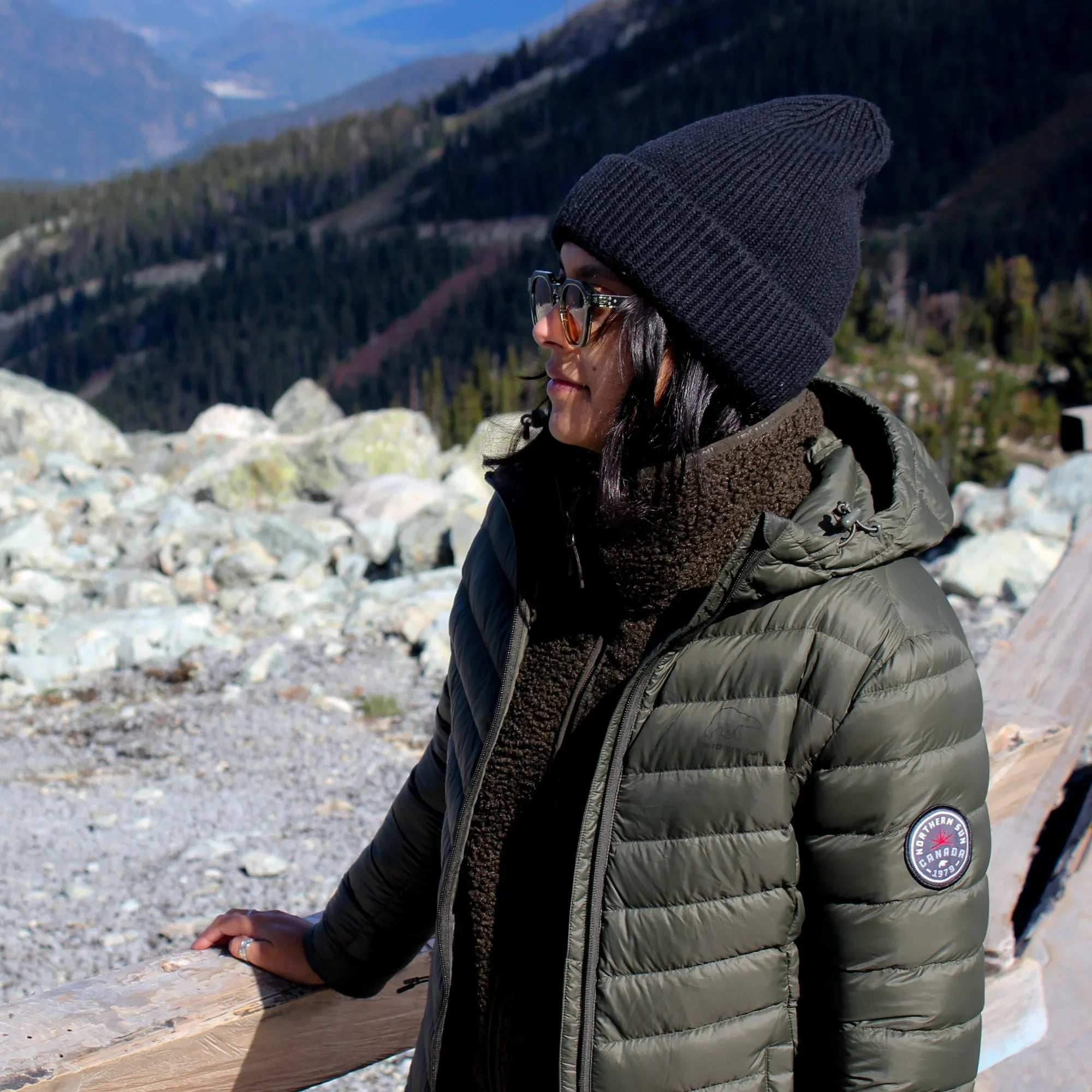 Woman in green packable lightweight down jacket and black beanie in mountain landscape