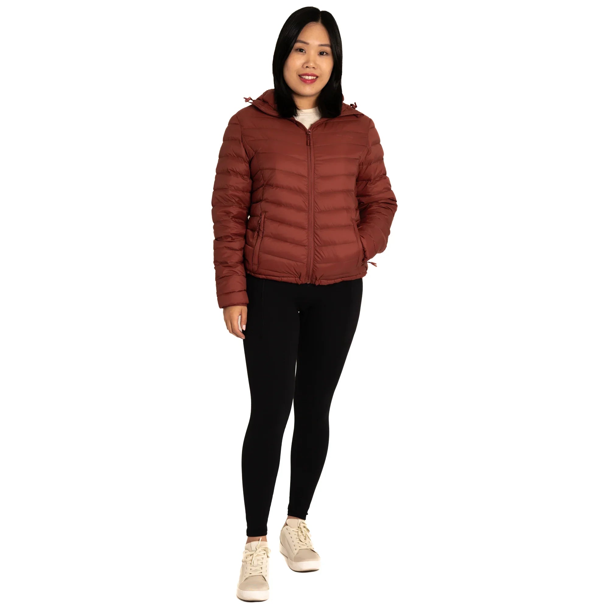 Woman wearing a brown puffer jacket, black leggings, and beige sneakers on white background