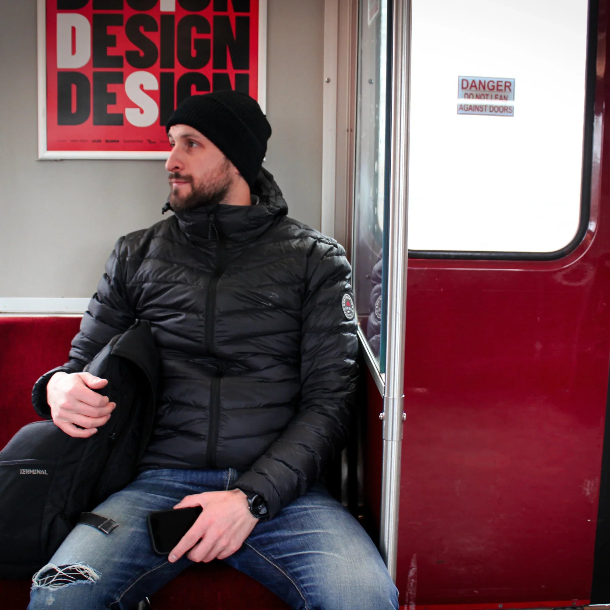 Man in black lightweight packable down jacket and beanie on city subway bench