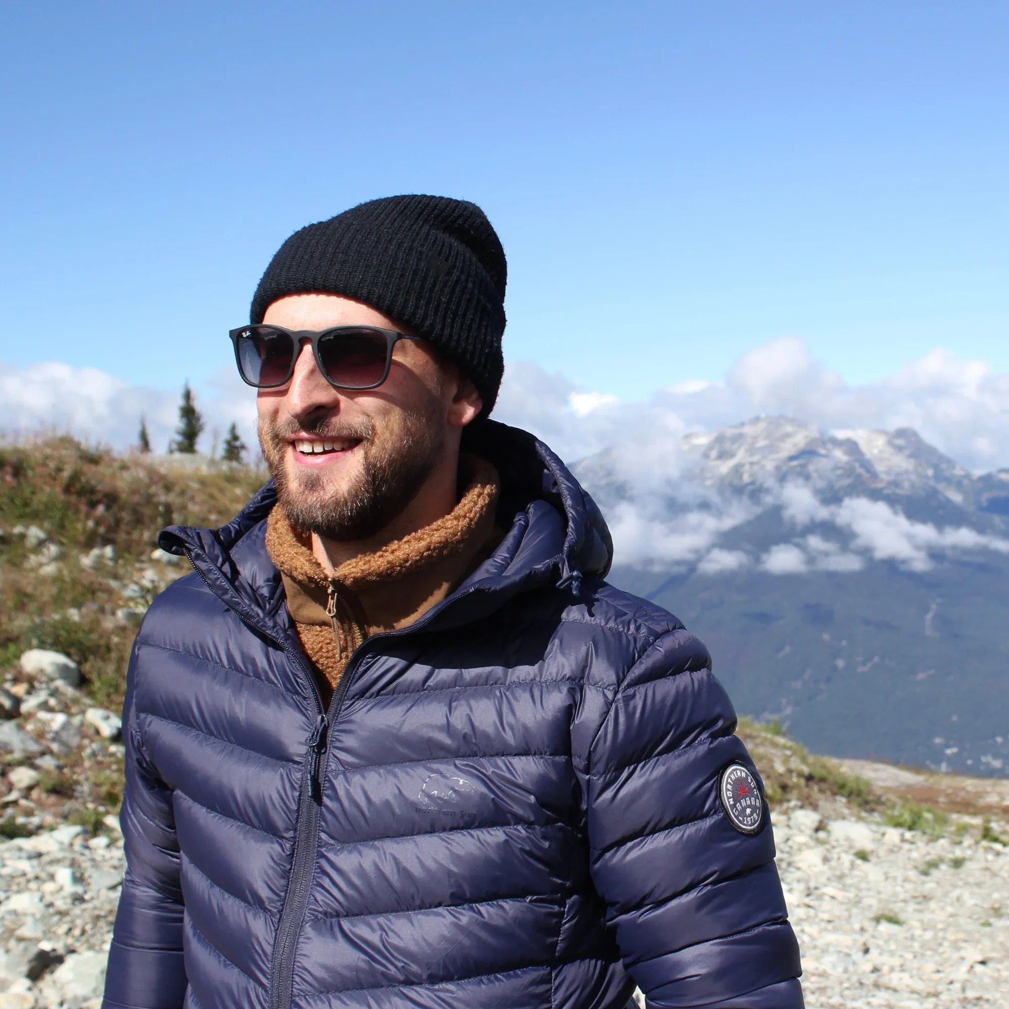Man wearing a navy lightweight packable down jacket and beanie on a mountain trail