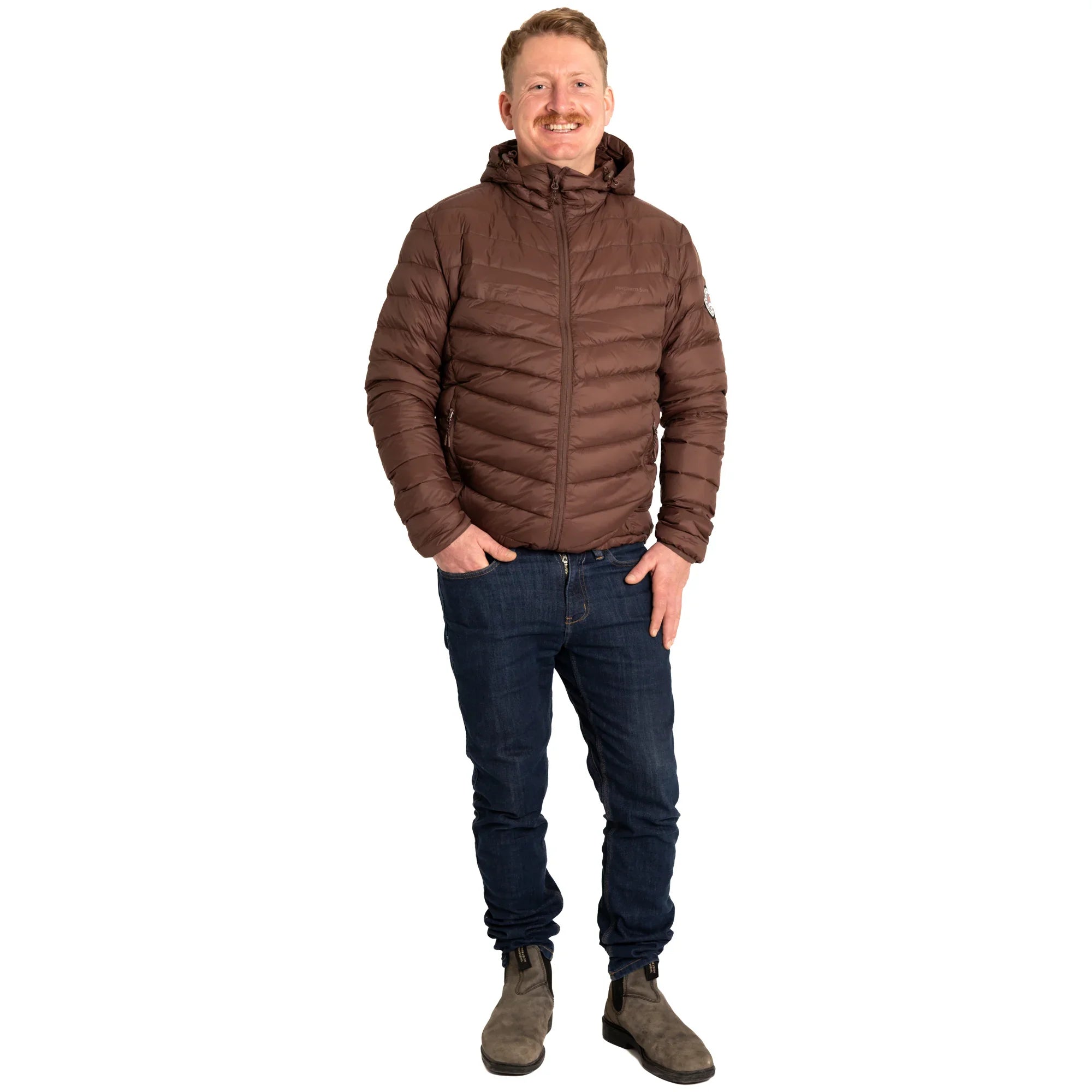 Man wearing a brown puffer jacket, blue jeans, and boots on a white background