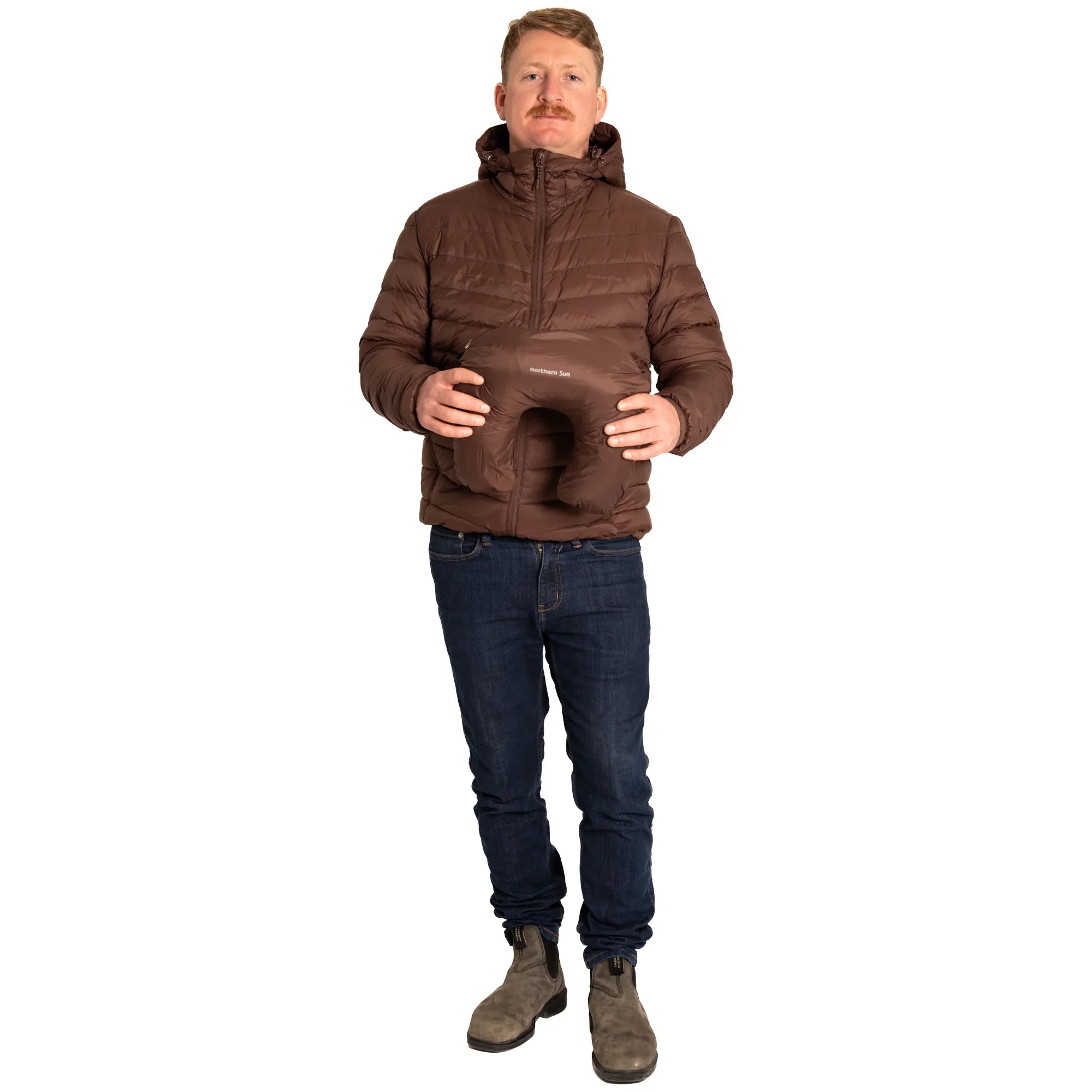 Man in brown puffer jacket holding brown travel pillow on white background