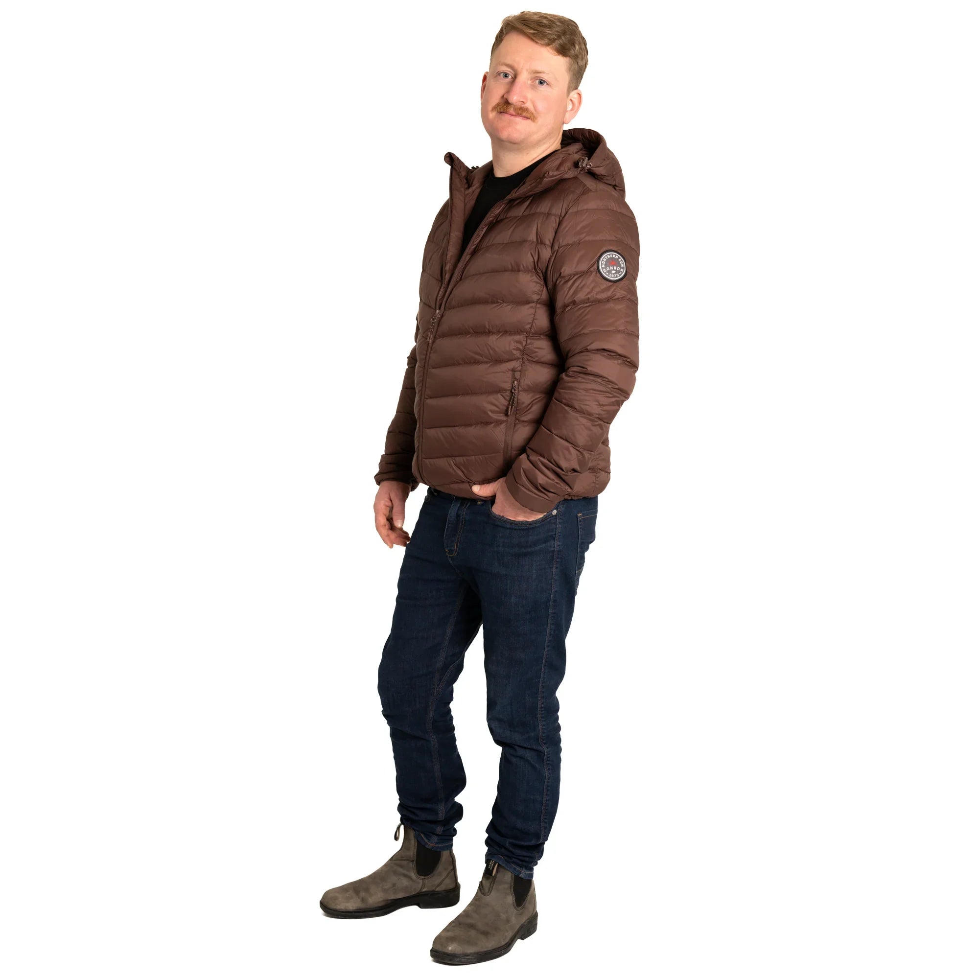 Man in brown puffer jacket with badge, blue jeans, and boots on white background