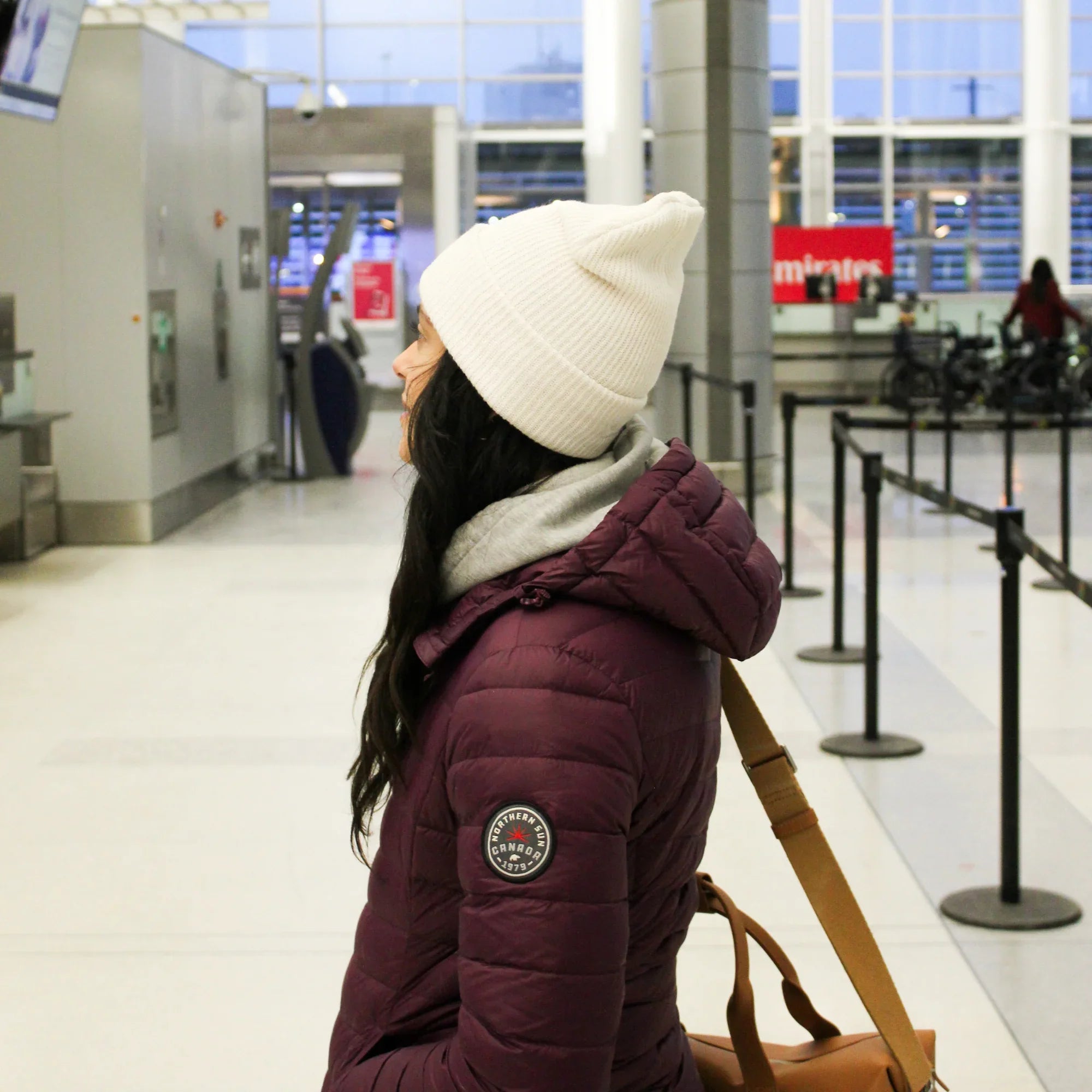 Woman in maroon packable lightweight down jacket and white beanie at airport terminal