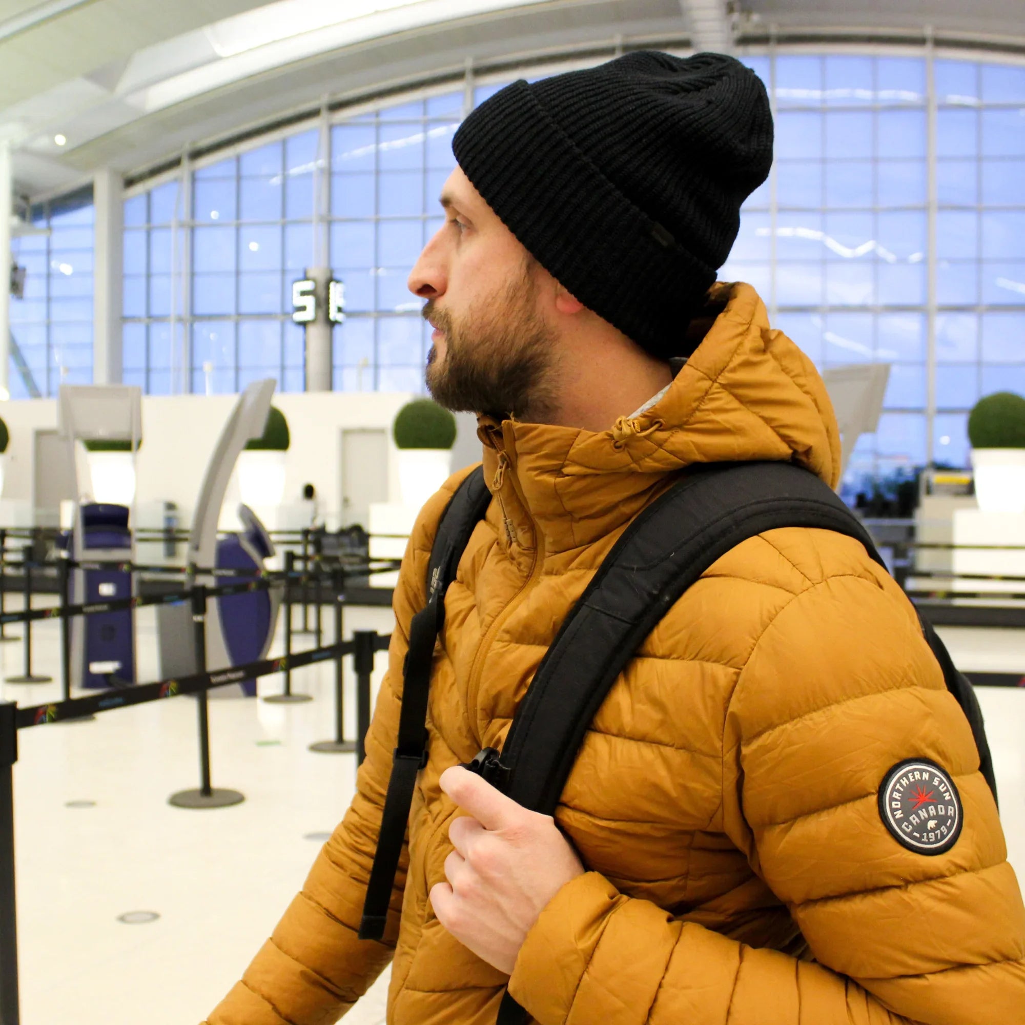Man wearing mustard Northern Sun men's packable down jacket with backpack in airport