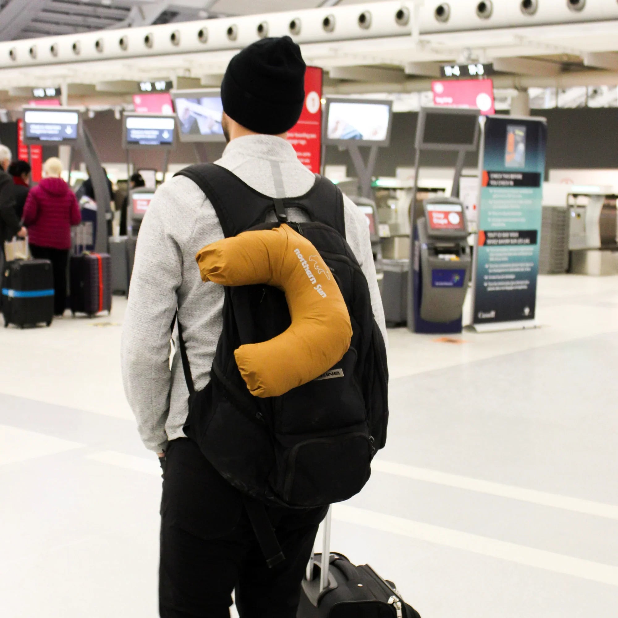Man at airport with a backpack and Northern Sun packable down jacket travel pillow