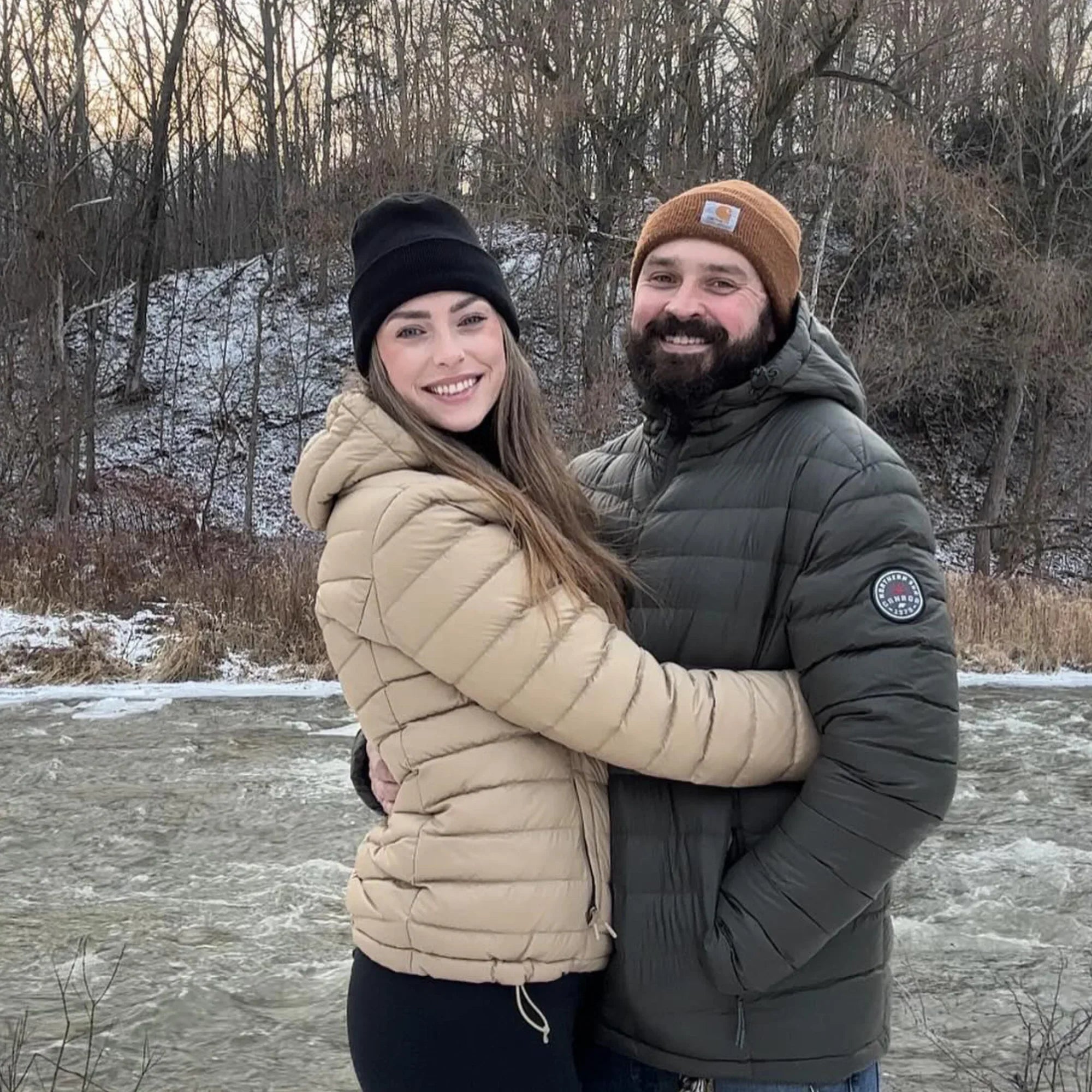 Woman in beige packable lightweight down jacket and man outdoors by a winter river