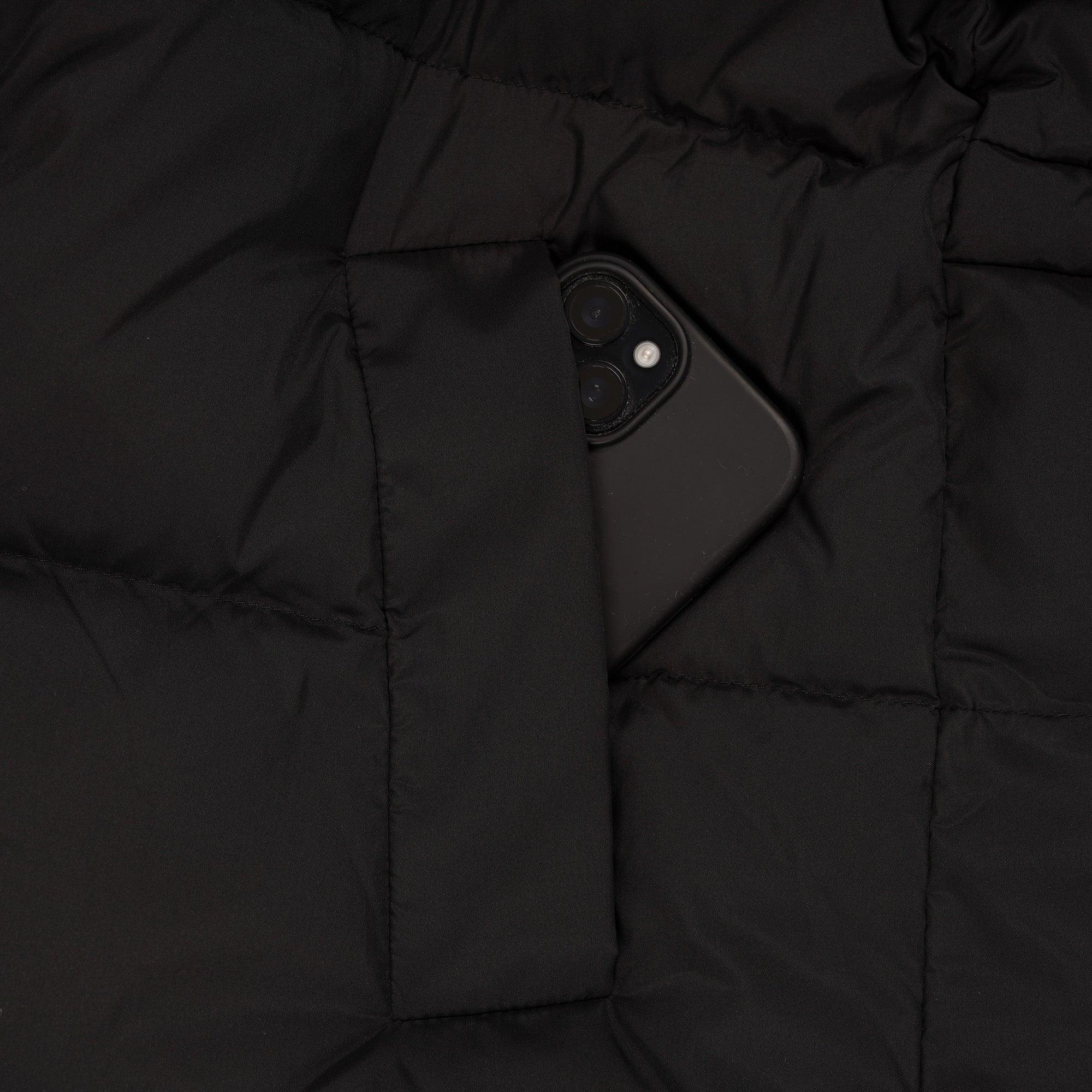 Black puffer jacket pocket holding a smartphone, quilted fabric texture visible