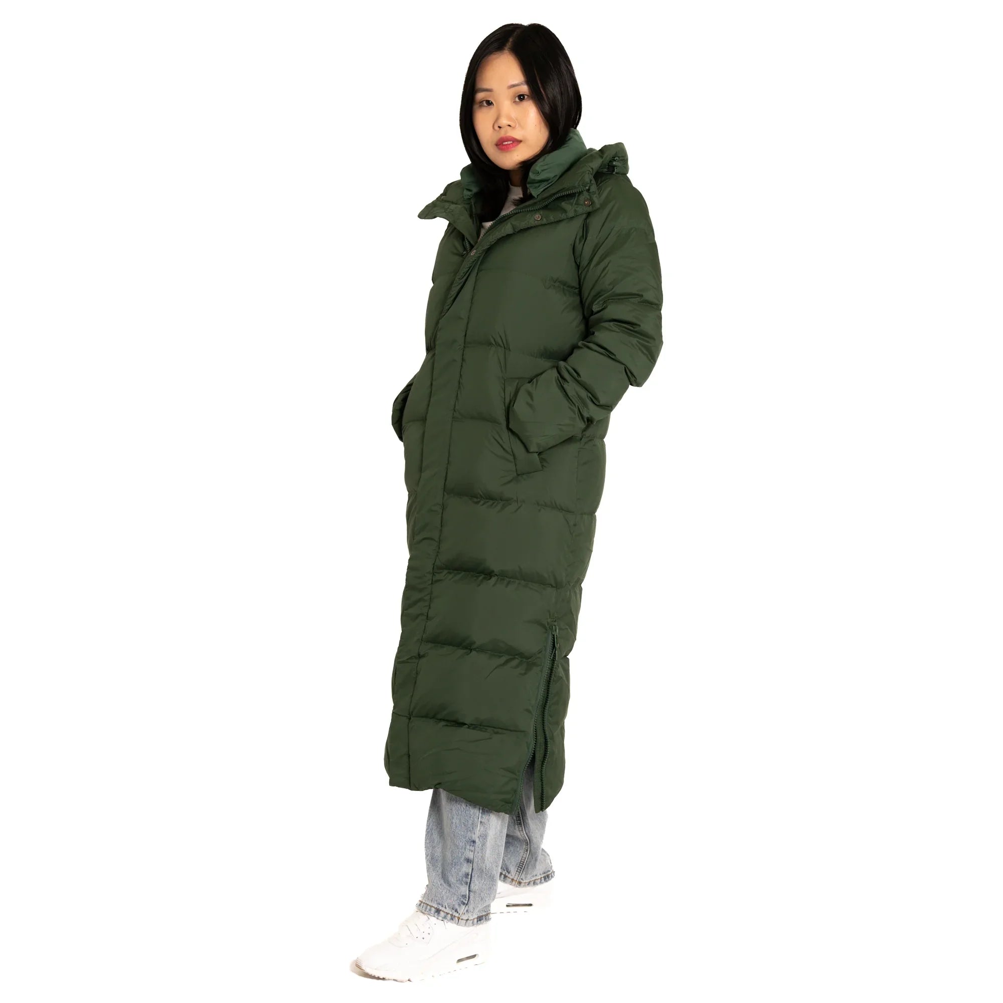 Woman wearing long green puffer coat, light jeans, and white sneakers on white background