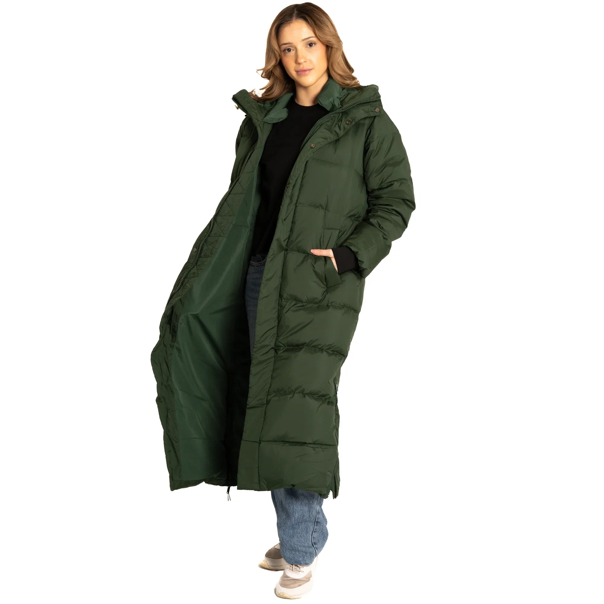 Woman wearing a long green puffer coat, blue jeans, and sneakers on white background