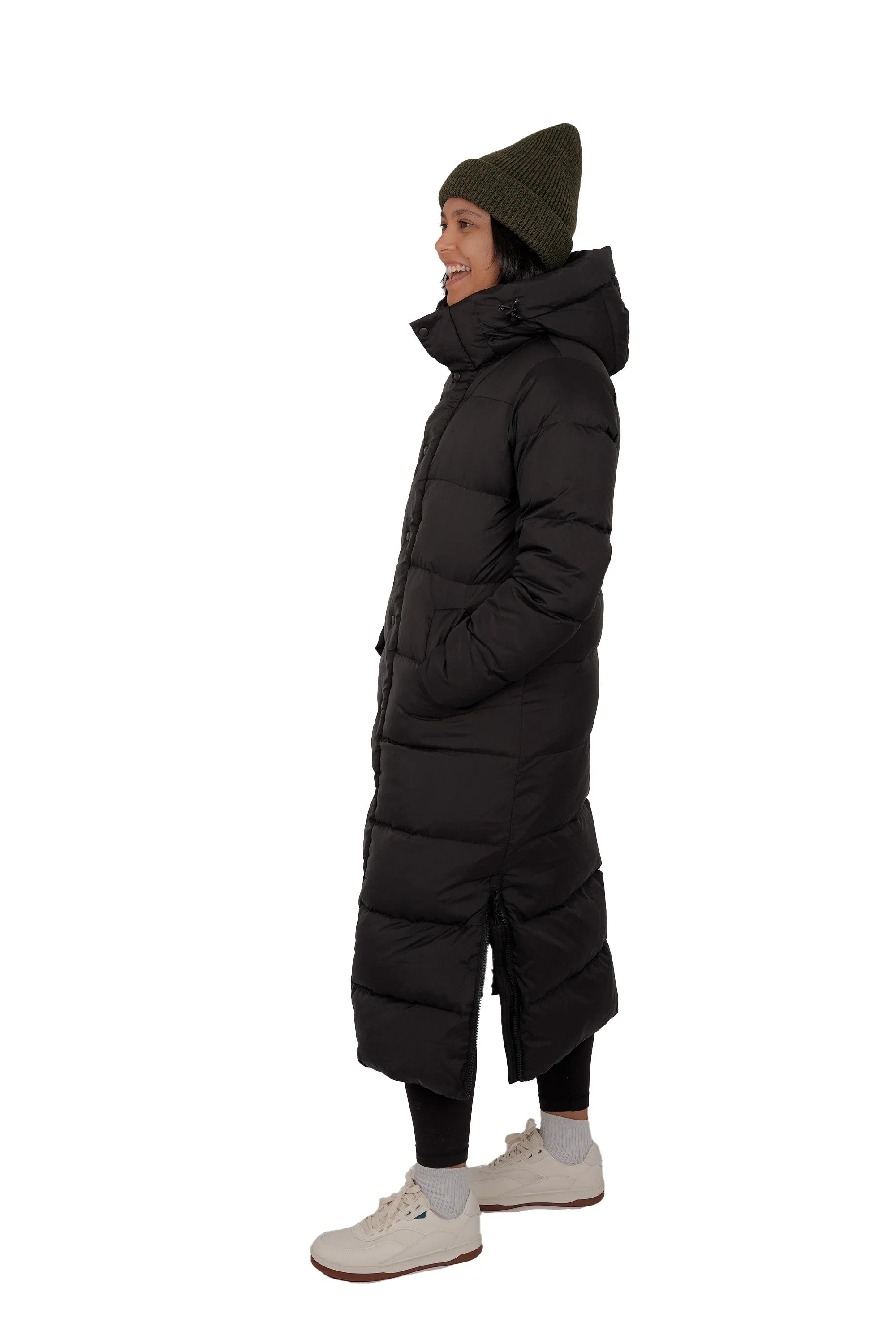 Woman in long black puffer coat, green knit beanie, and white sneakers, side view