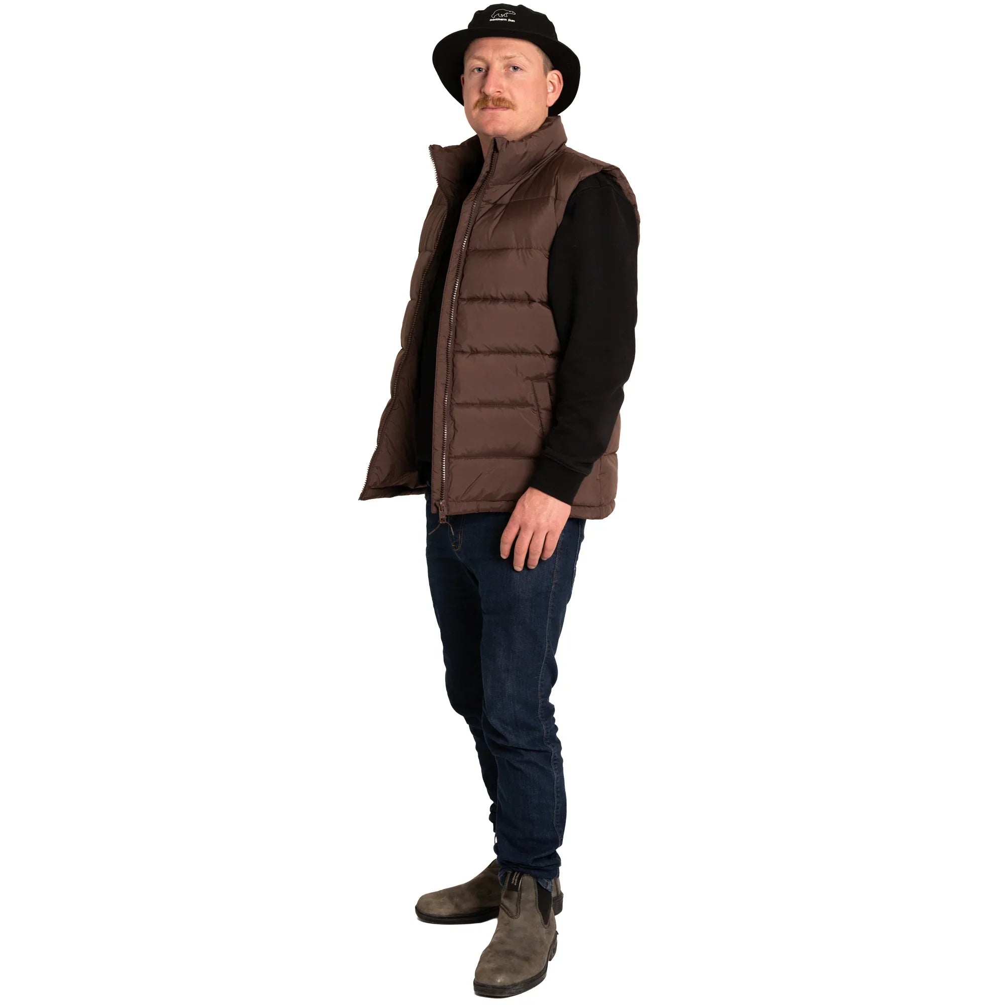 Man in a brown puffer vest, black hat, jeans, and boots on white background