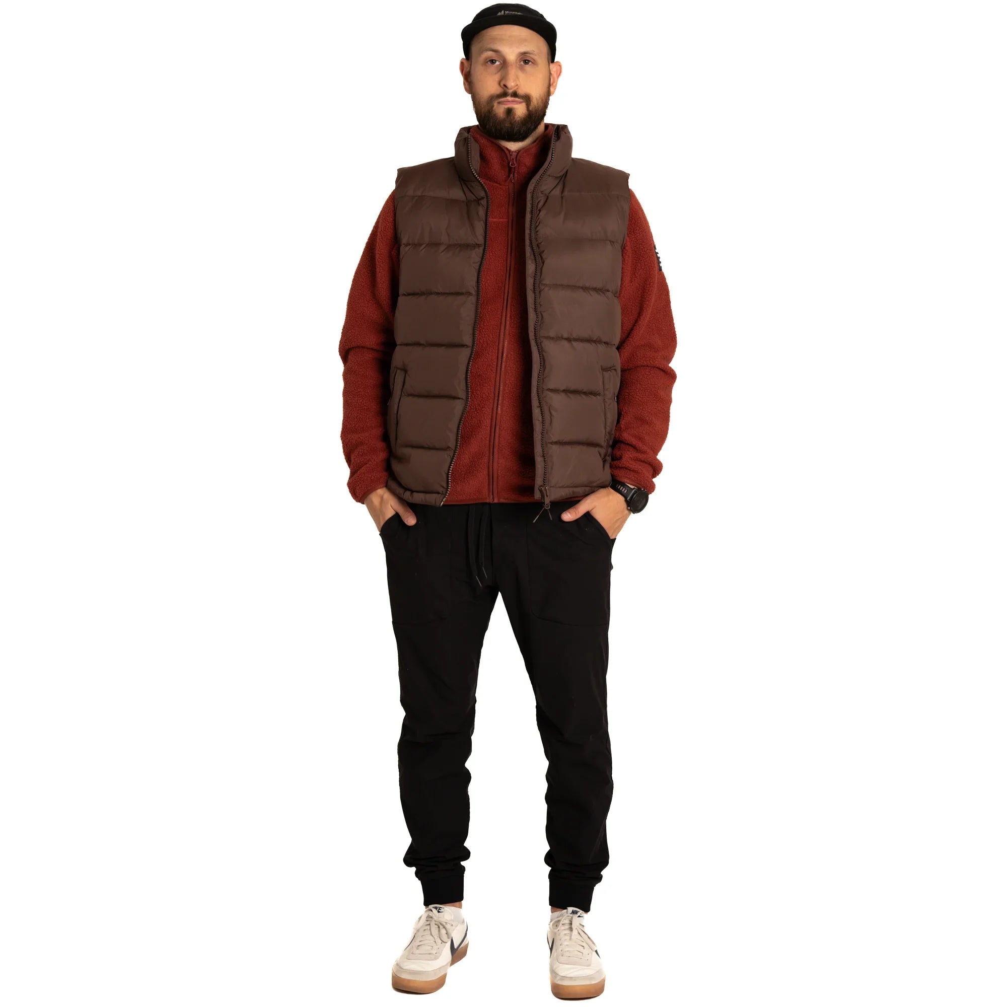 Man wearing brown puffer vest, red fleece jacket, black joggers, and white sneakers