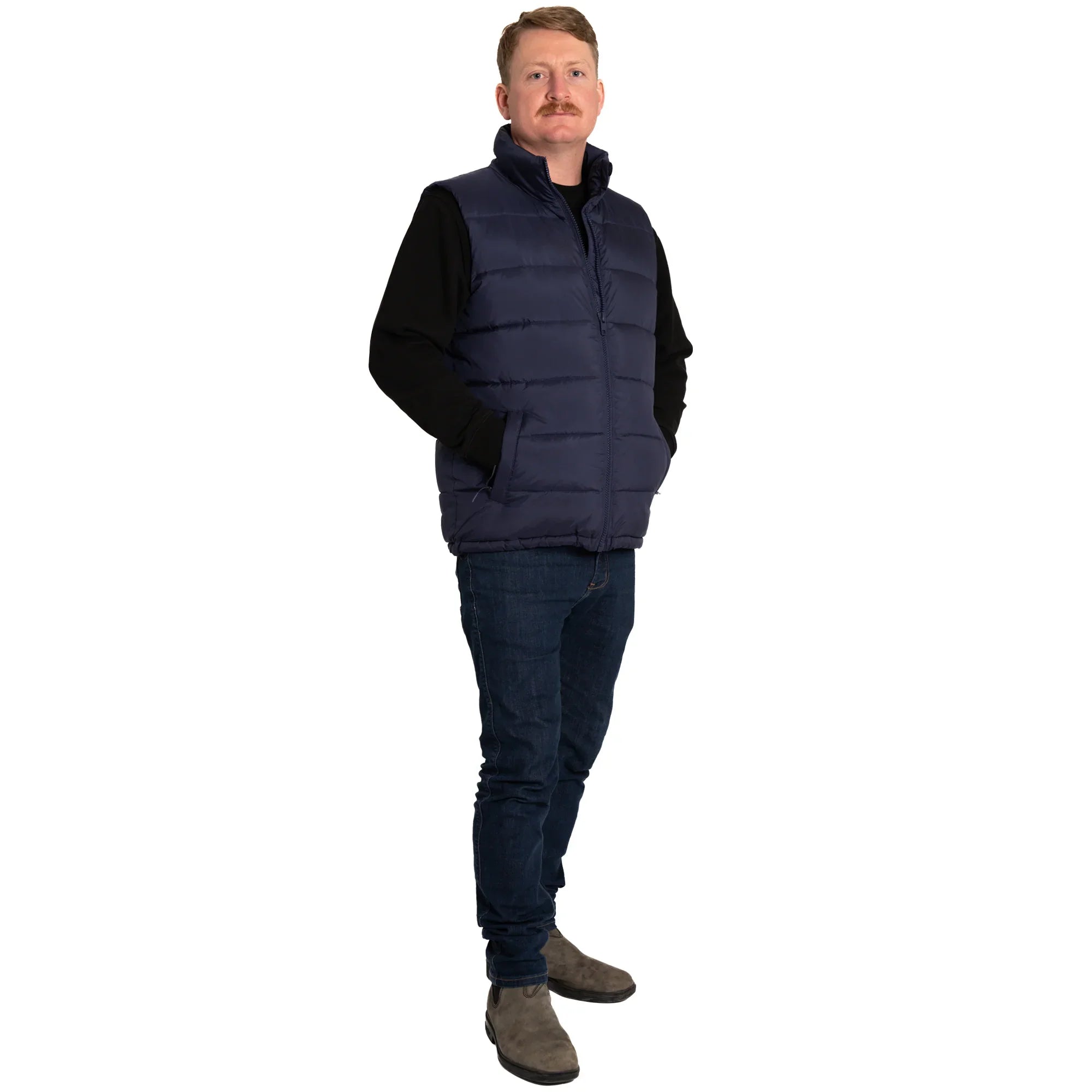 Man wearing navy puffer vest, black shirt, jeans and boots on white background