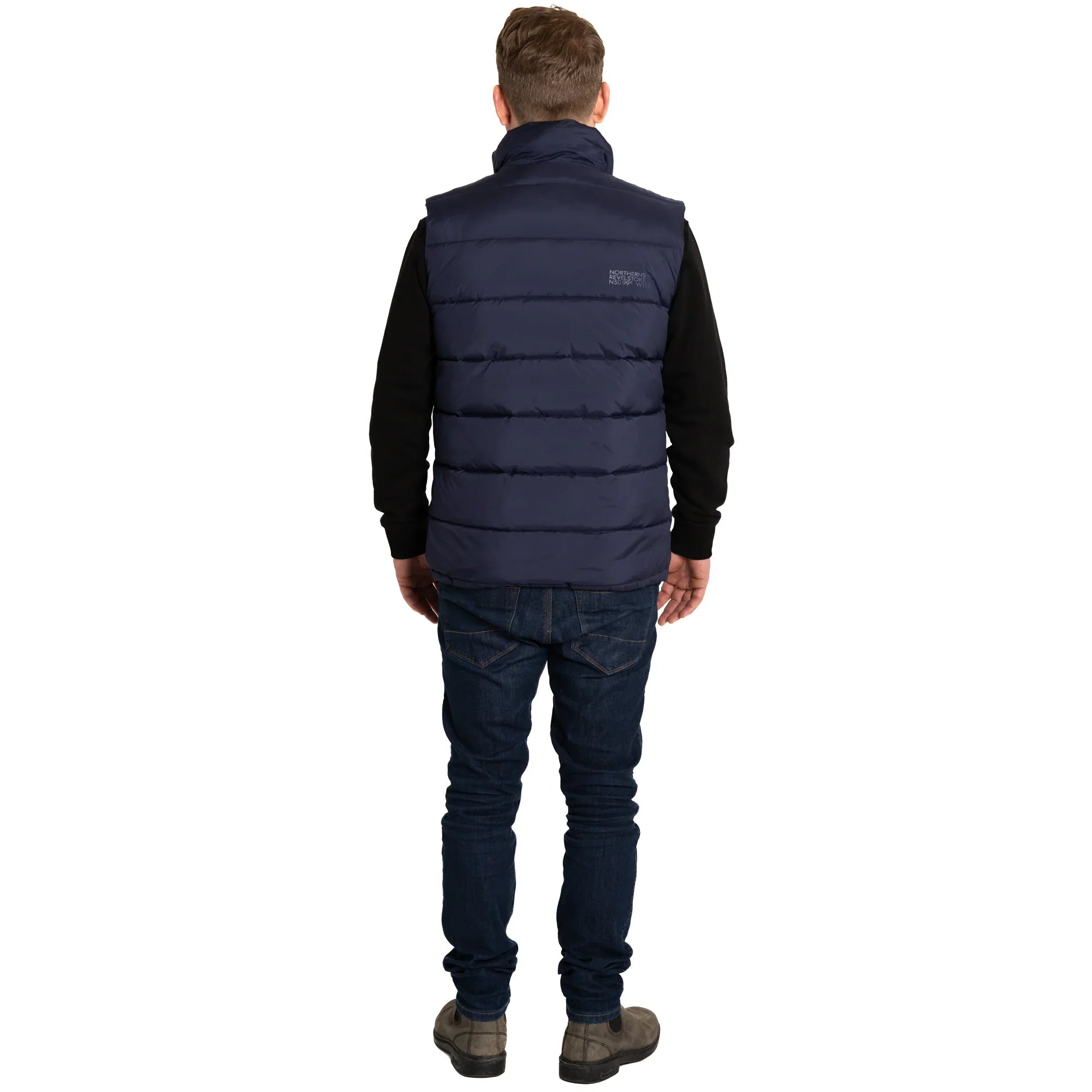 Man in navy blue puffer vest, black sweatshirt, jeans, and boots standing on white background