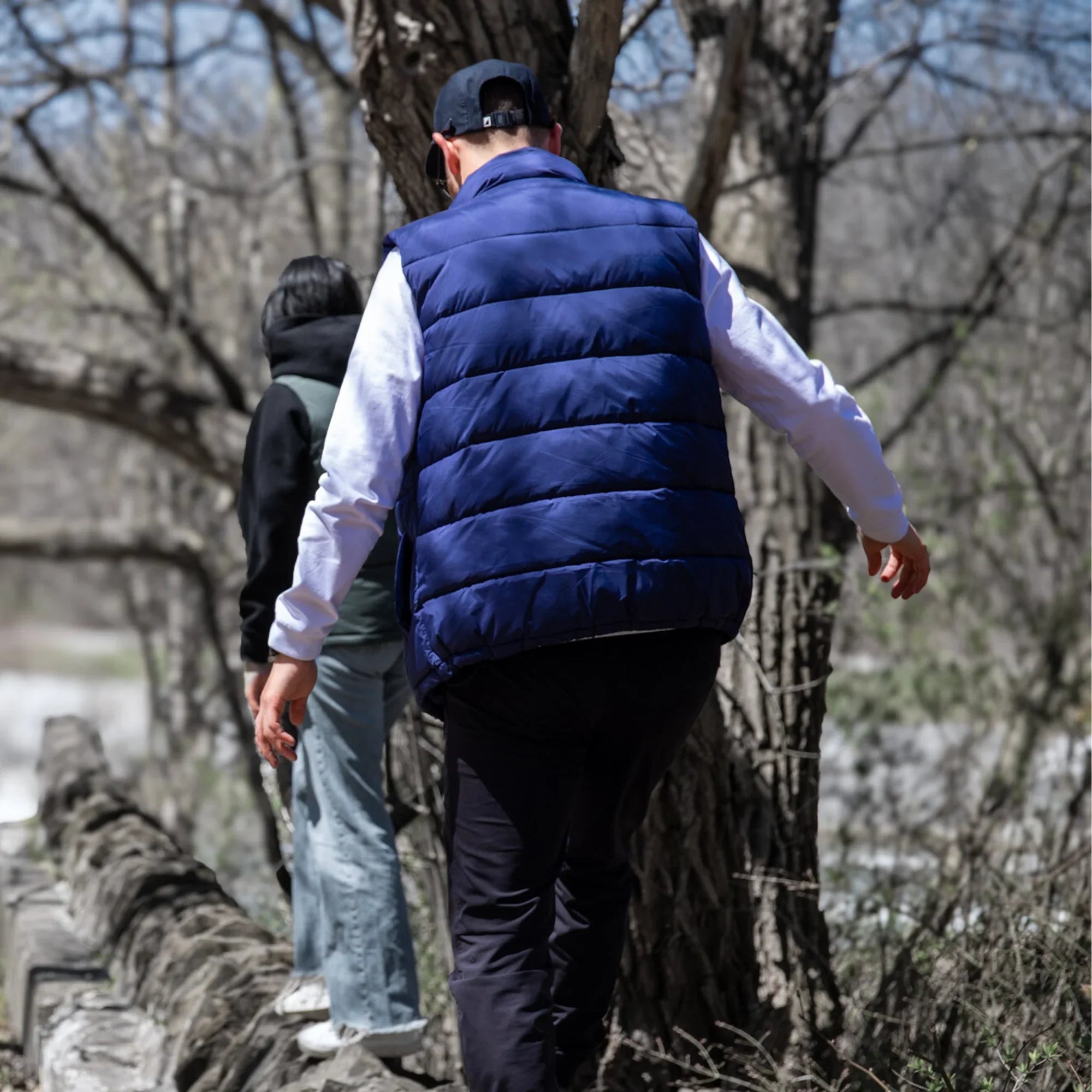 Man in blue puffer vest hiking outdoors on a rocky trail in a forest
