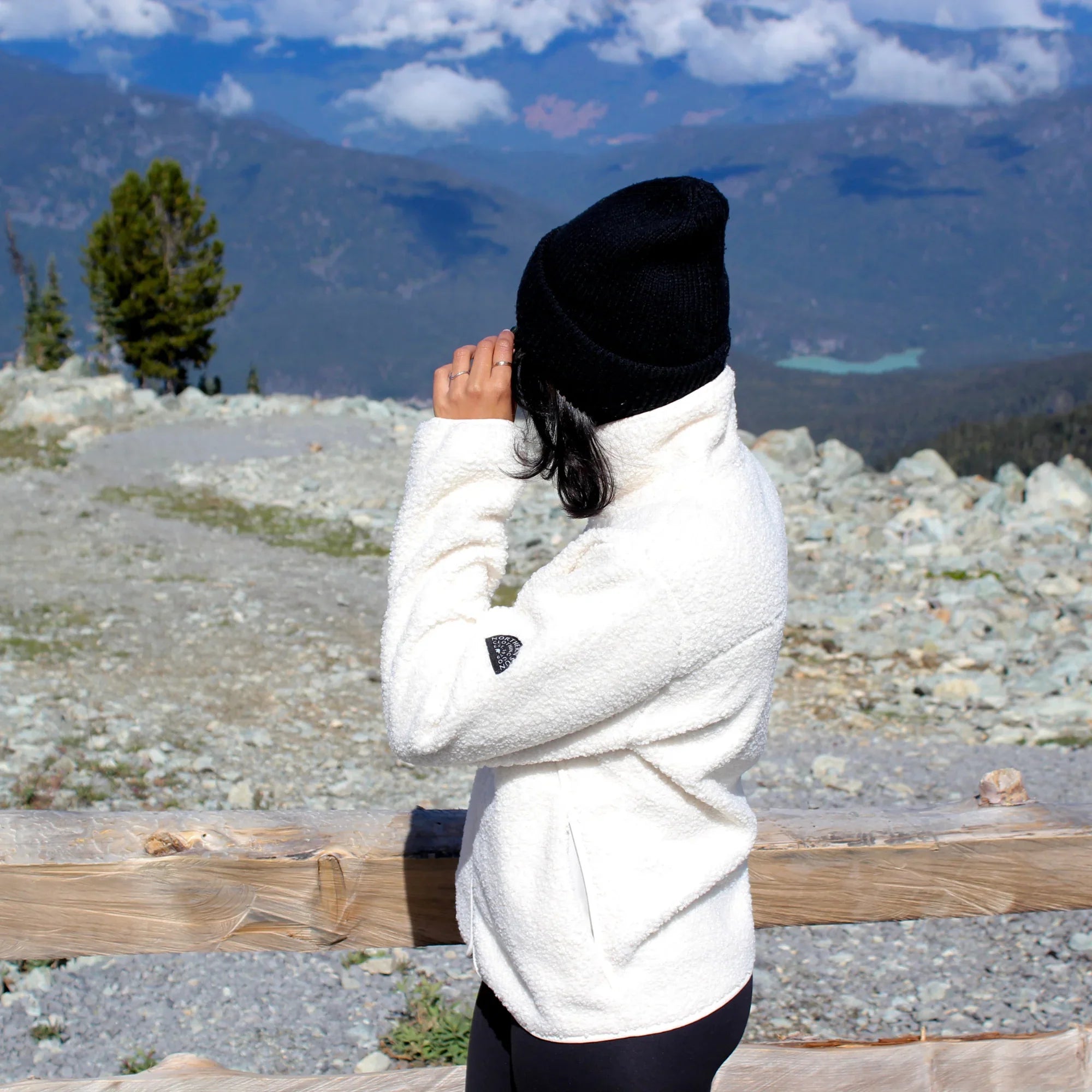 Woman wearing white teddy fleece jacket and black beanie in mountain outdoor setting