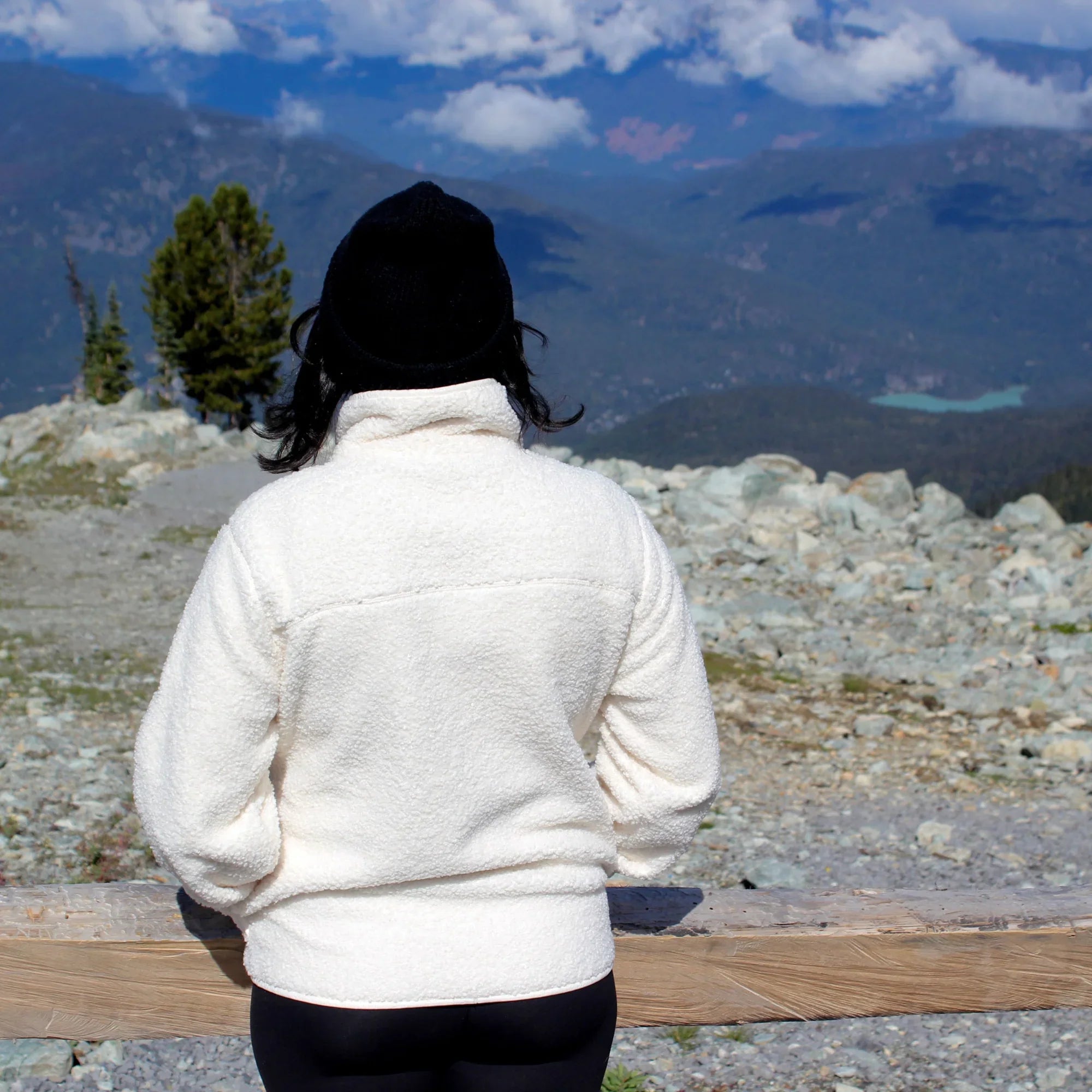 Woman in white teddy fleece jacket and black beanie standing outdoors on rocky mountain trail